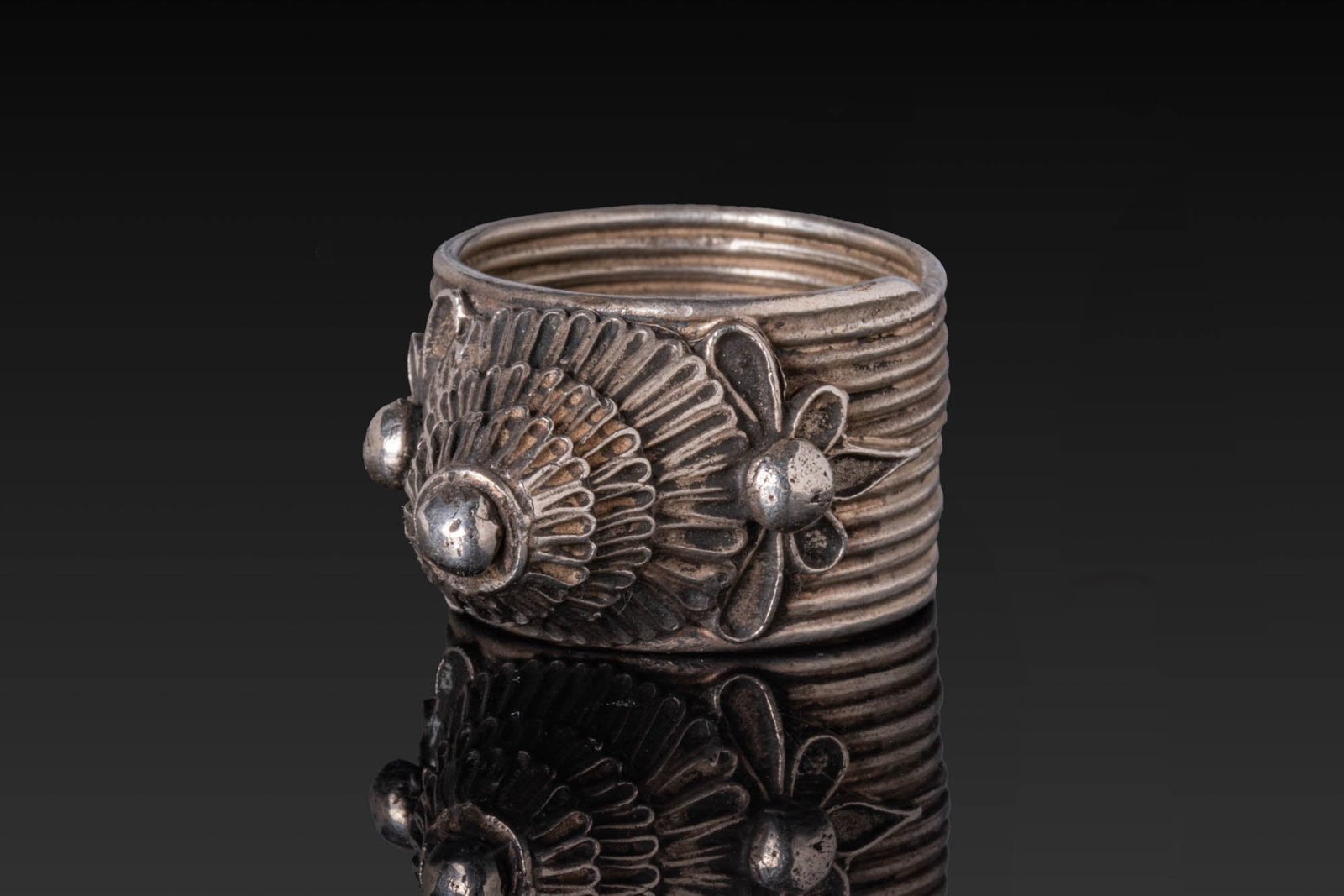 OTTOMAN OR QAJAR SILVER-GILT RING WITH CONICAL BEZEL: Ca. AD 1800 - 1900. A silver ring with a wide, ribbed hoop and a high, stepped conical bezel with radiating fluting, capped by a hemispherical knop. Two applied wire floral motifs with pellet centres