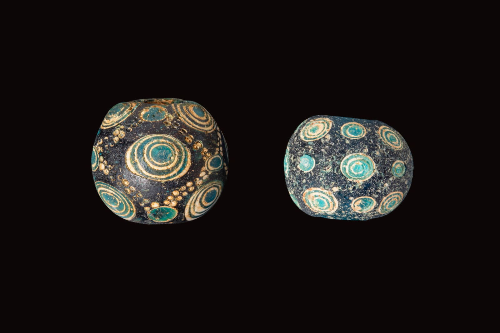 PAIR OF ANCIENT CHINESE GLASS EYE BEADS: Ca. 770 - 256 BC. A pair of glass beads, each a large globular bead in blue with applied concentric eye motifs in turquoise and white, linked by diagonal trails of closely spaced white dots. For simil