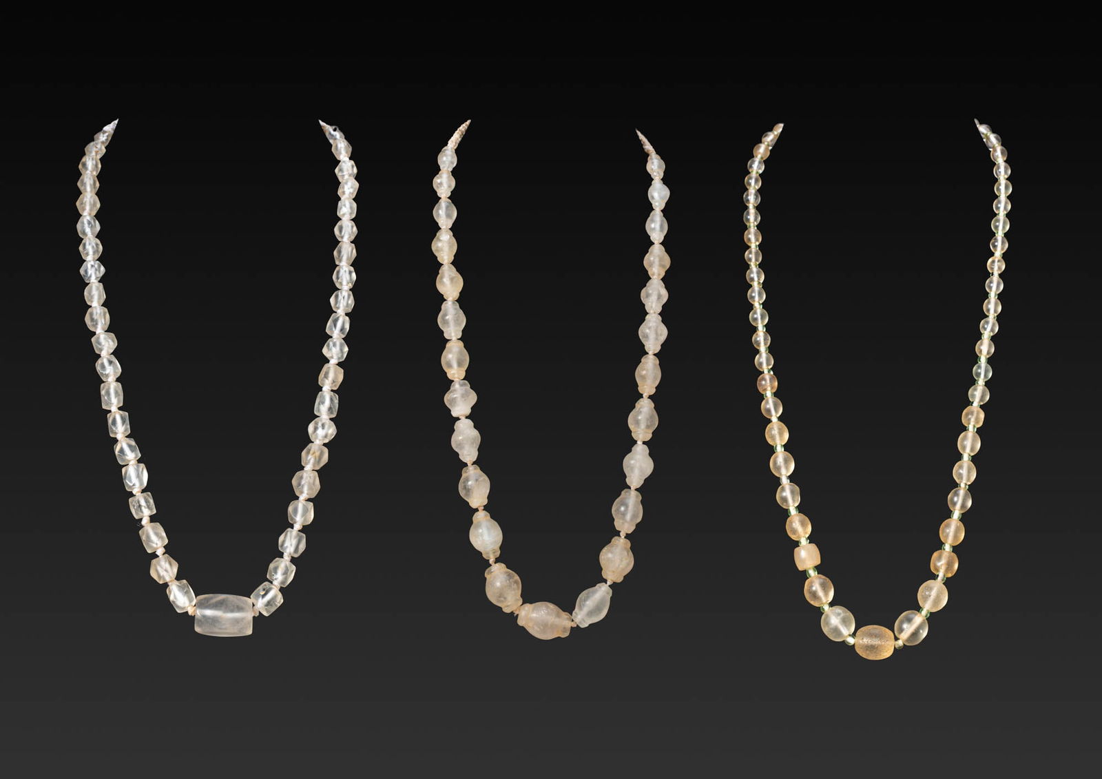 COLLECTION OF WESTERN ASIATIC ROCK CRYSTAL BEADS: Ca. 2nd - 1st millennium BC. A collection of three necklaces, each strung with rock crystal beads, including: a strand of large barrel beads with constricted ends; a strand of faceted polyhedral beads