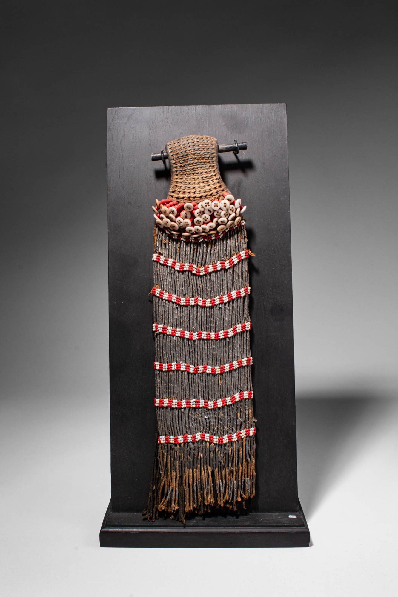 CAMEROON FEATHER HAT: Ca. late 19th century AD. >A feather hat constructed from woven fibre forming a structured upper section, the headdress is richly adorned with rows of small shells and bands of red and white beads.