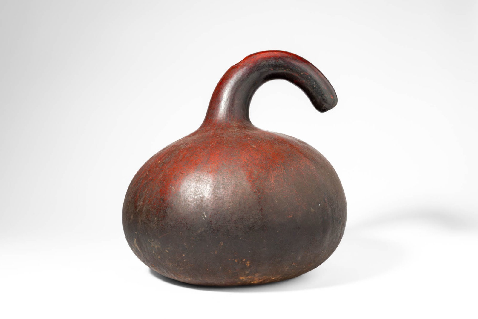 CAMEROON PALM WINE GOURD VESSEL: Ca. 20th century AD. >A palm wine vessel formed from a natural gourd, its rounded body rising to a distinctive arched neck that curves forward to form a pouring spout. The elegant, continuous curve