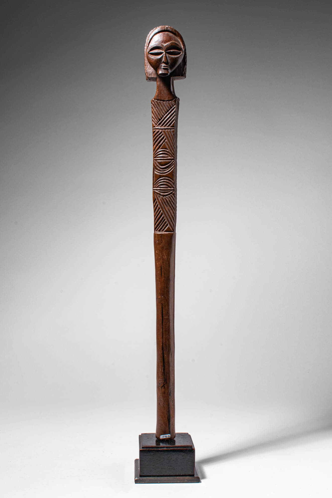 CHOKWE WOODEN STAFF: Angola, Ca. late 19th - early 20th century AD. >A long staff surmounted by a carved globular female elderly head with stylised facial features, including almond-shaped eyes, a narrow nose, and a small