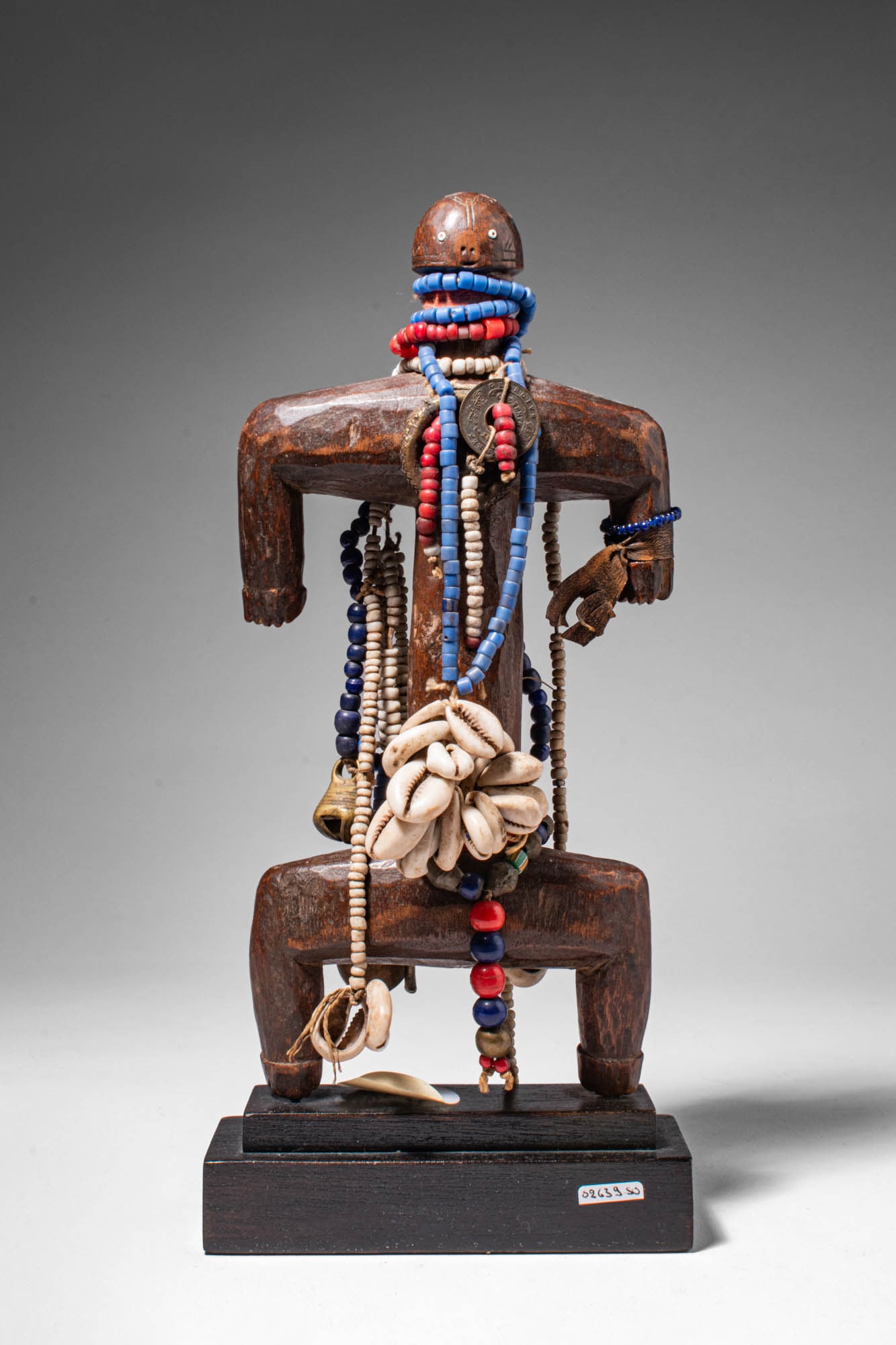 CAMEROON DOWAYO / NAMJI DOLL: Ca. 20th century AD. >A standing figure with outstretched horizontal arms and bent legs, the wooden body is decorated with numerous strands of trade beads draped across the neck and torso. Shells, pen