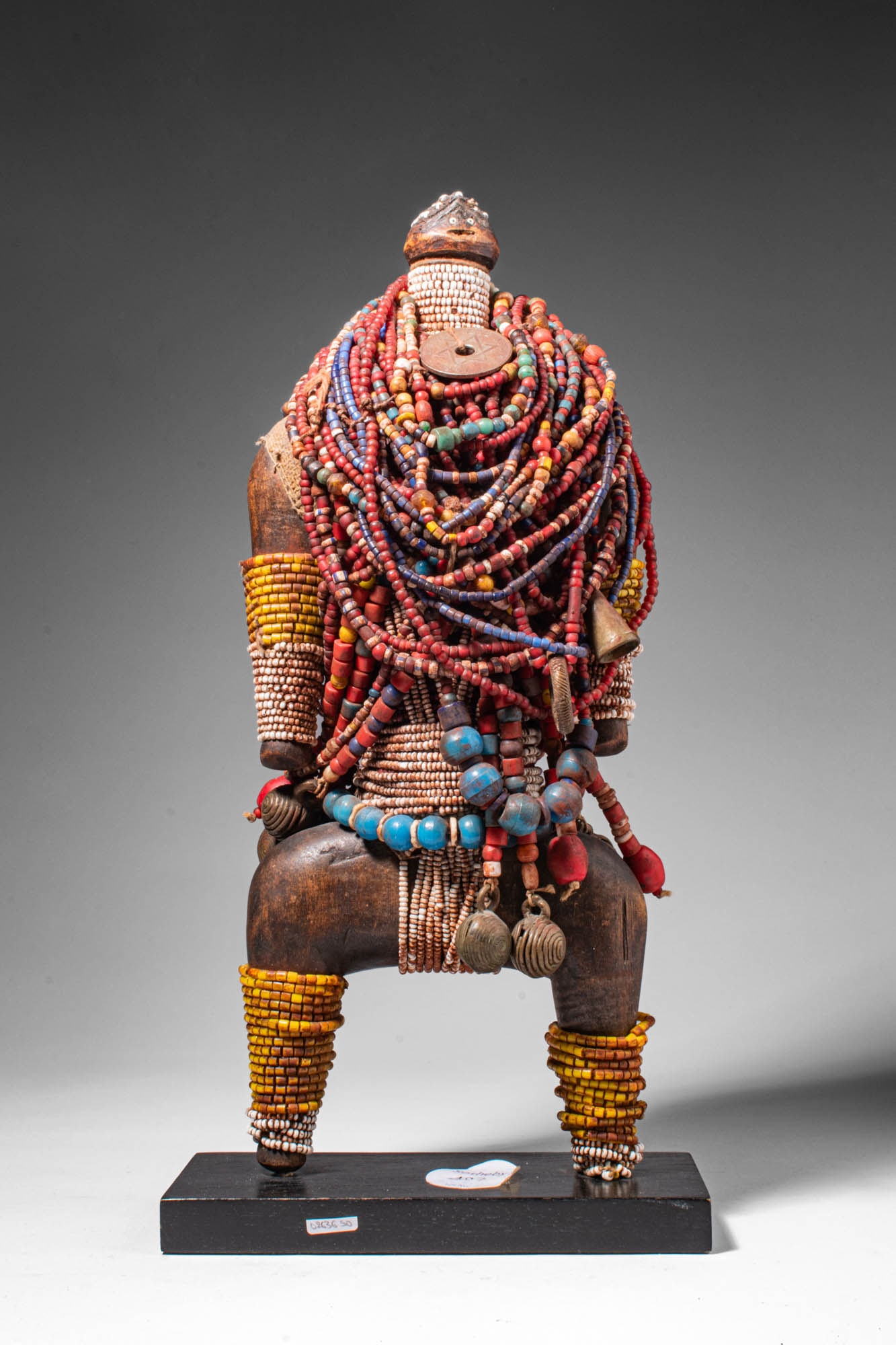 CAMEROON NAMJI DOLL: Ca. 20th century AD. >A standing figure with a small head and broad hips, the doll is heavily adorned with numerous strands of multicoloured beads draped across the torso and waist. Additional beadwor