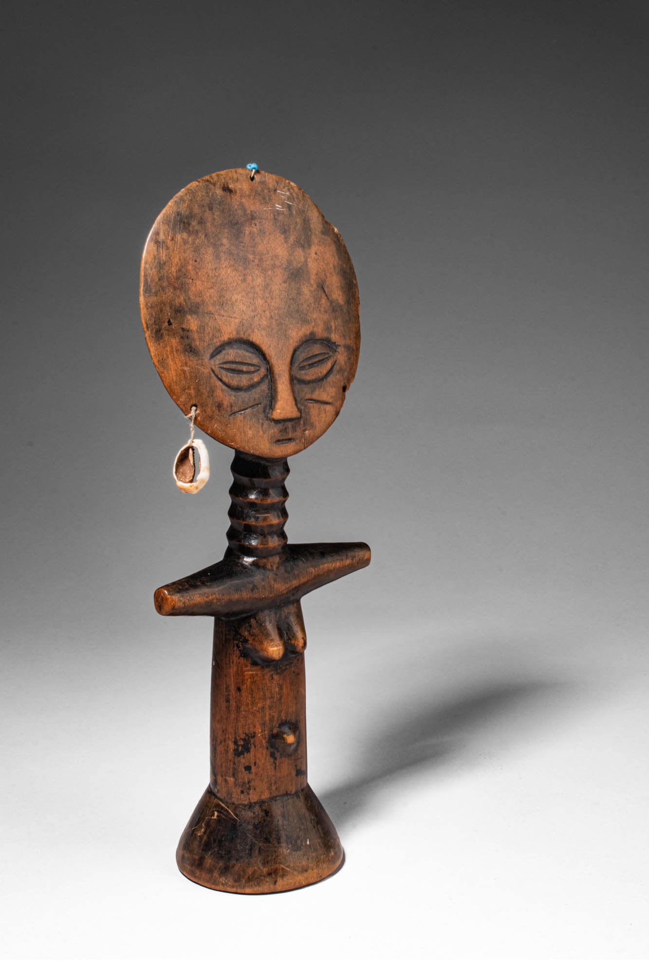 WOODEN AKUA'BA DOLL: Ca. 19th - 20th century AD. >A wooden Akua'ba doll carved in the characteristic Akuaba form, the figure features a large circular head above a slender cylindrical body with short horizontal arms. The