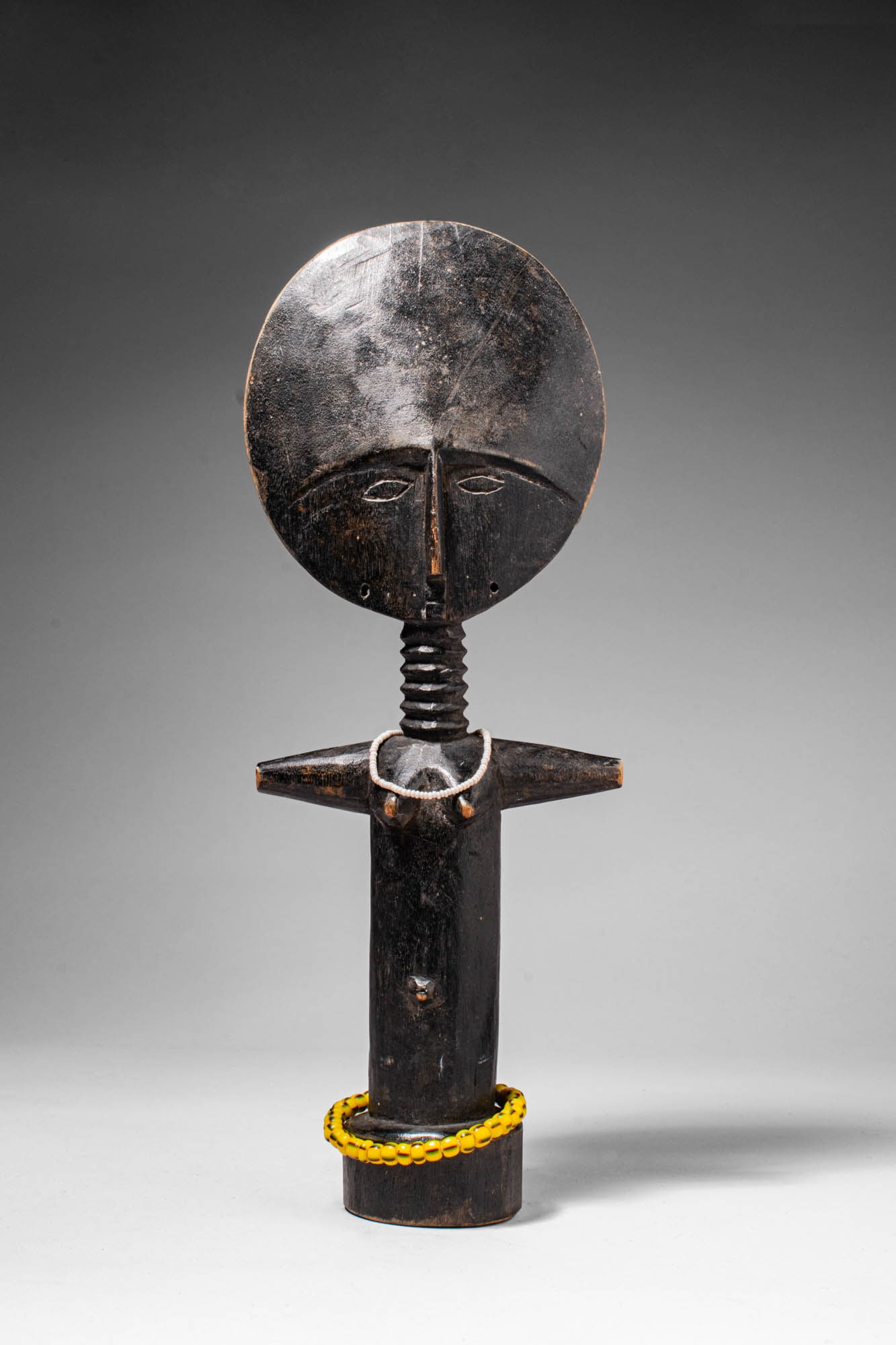 ASHANTI WOOD AKUABA DOLL: Ca. early 20th century AD. >A beautiful Akua'ba doll carved in the canonical form. The figure is distinguished by its large, disc-shaped head, rising above a slender cylindrical body with short outrea