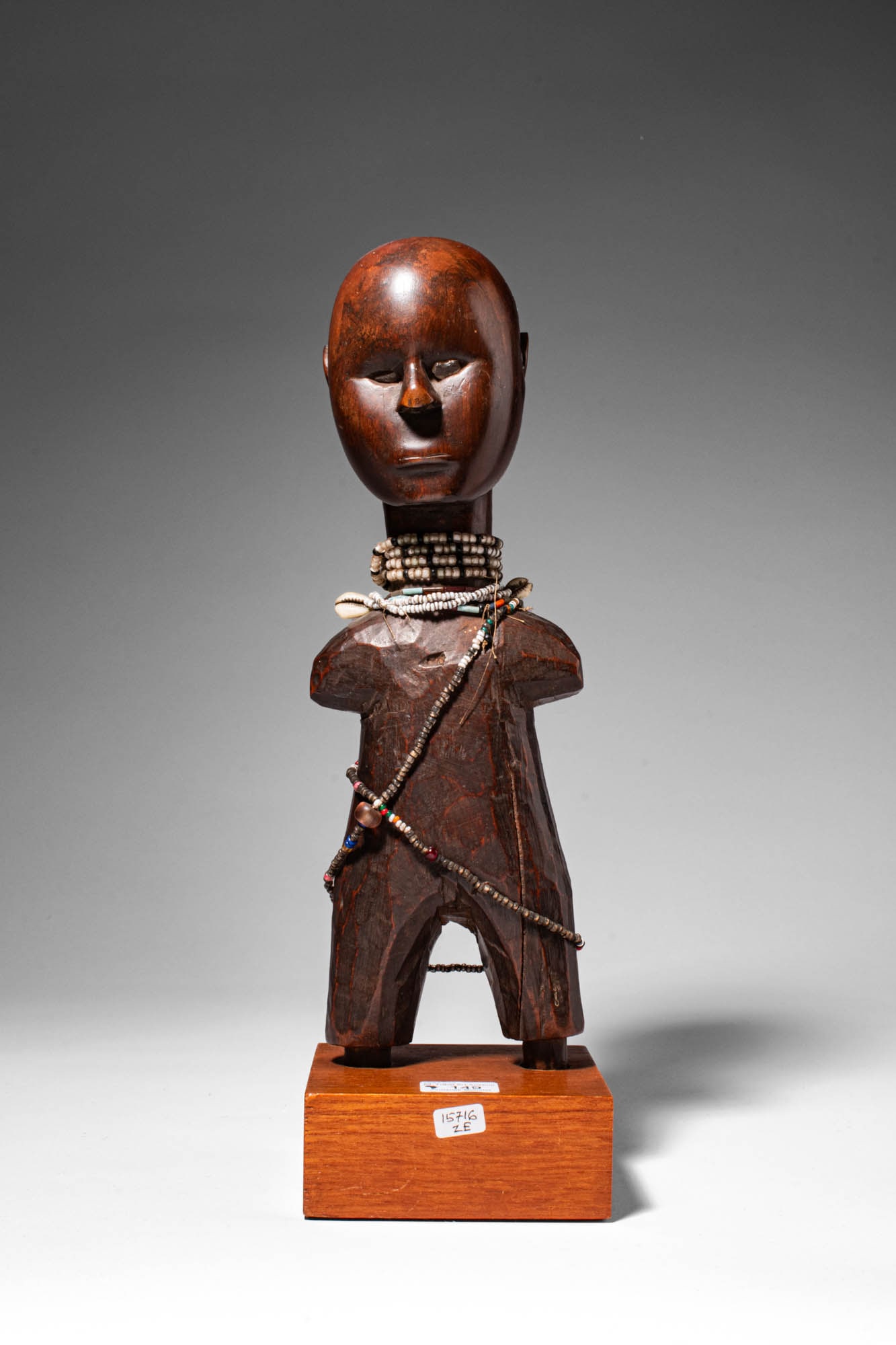 KAMBA WOODEN STANDING FIGURE: Ca. 20th century AD. >A fine Kamba wooden standing figure carved with a slender, simplified body and short projecting arms, the sculpture is distinguished by its large, smoothly modelled head with sof