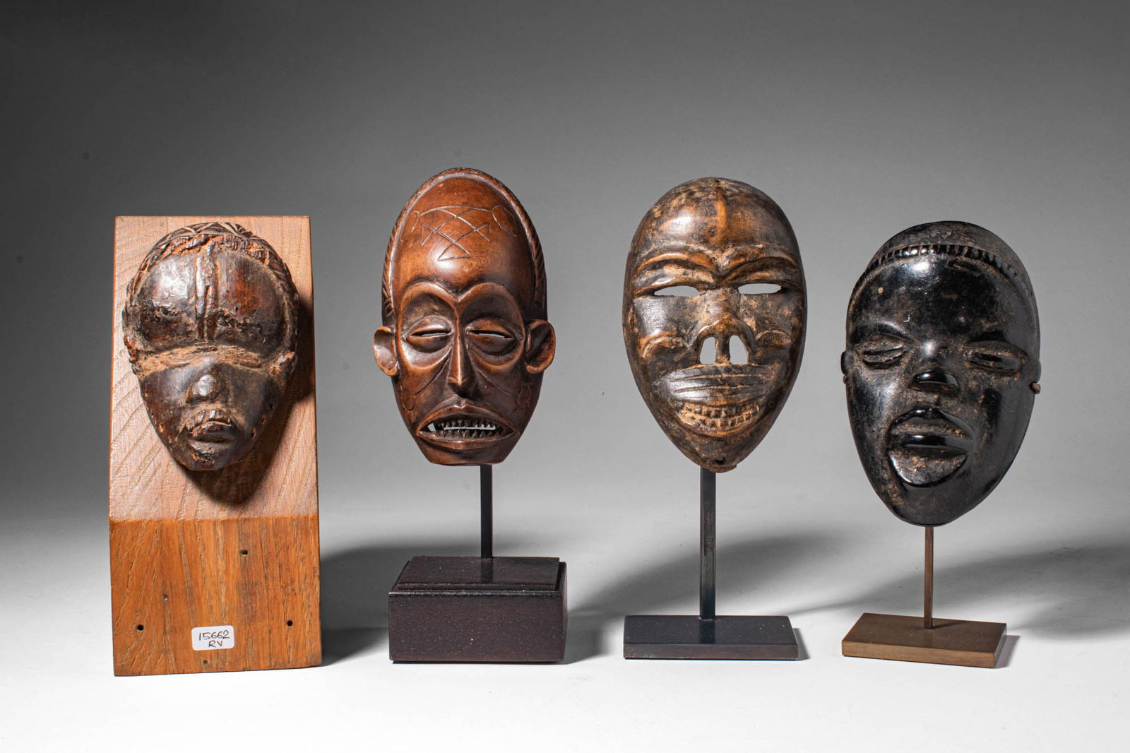 GROUP OF DAN PASSPORT MASKS: Ca. 19th - 20th century AD. >A group of four miniature carved wooden masks with elongated oval faces and stylised features, including almond-shaped eyes, pronounced noses and incised coiffures. Three