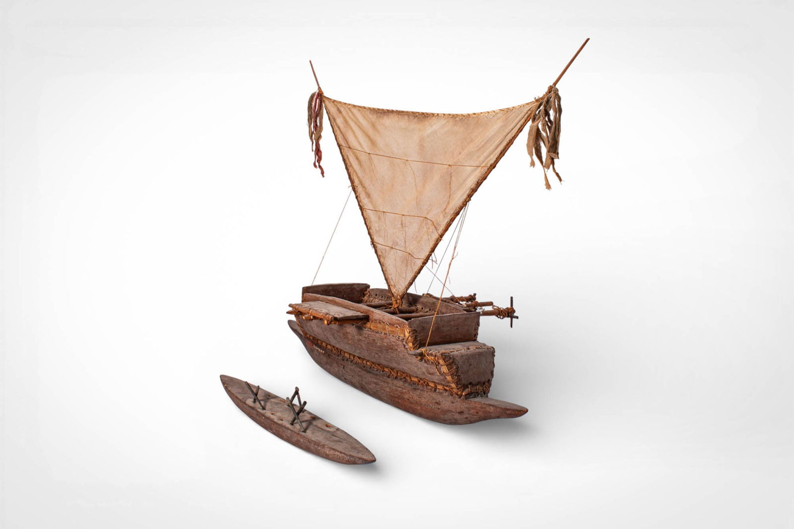 PAIR OF PACIFIC ISLAND CANOE MODELS: Ca. 19th century AD. >A pair of canoe models carved from wood and constructed with miniature elements reflecting traditional Pacific watercraft. The larger model features a broad hull with a triangula