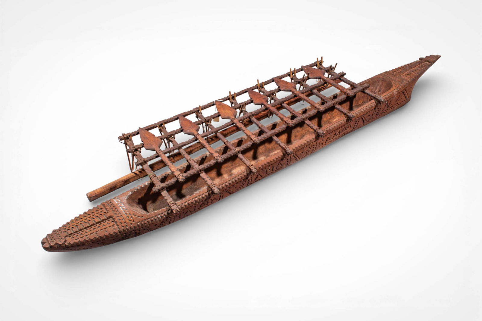 OCEANIC CANOE MODEL: Ca. 20th century AD. >A carved wooden canoe modelled in the form of an elongated boat, its surface decorated with incised geometric patterns across the hull. The open central section supports a raised