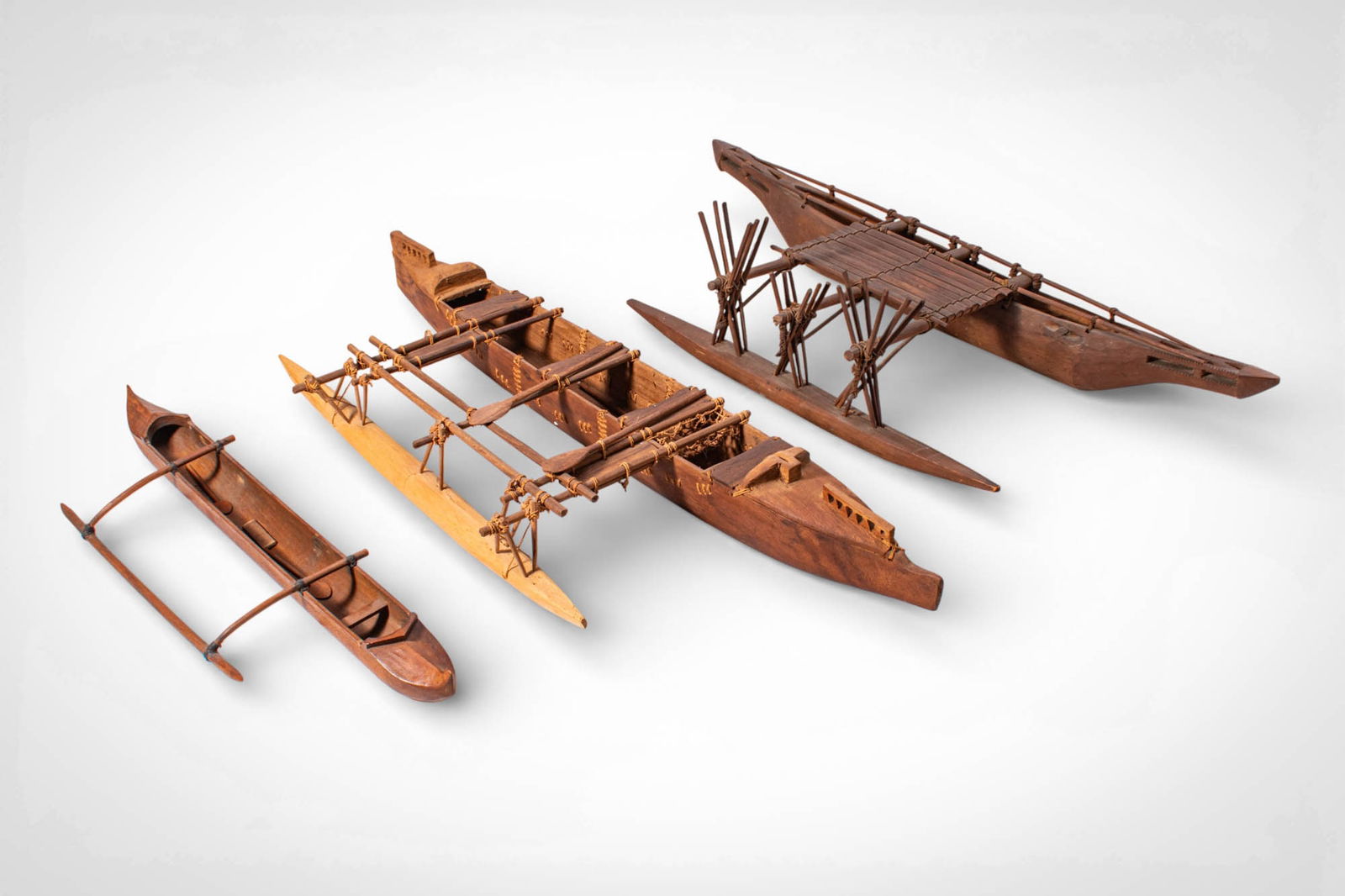 GROUP OF POLYNESIAN CANOE MODELS: Ca. 20th century AD. >A group of three Polynesian canoe models, each carved from wood and constructed with miniature architectural elements reflecting traditional seafaring vessels of the Pacific. The
