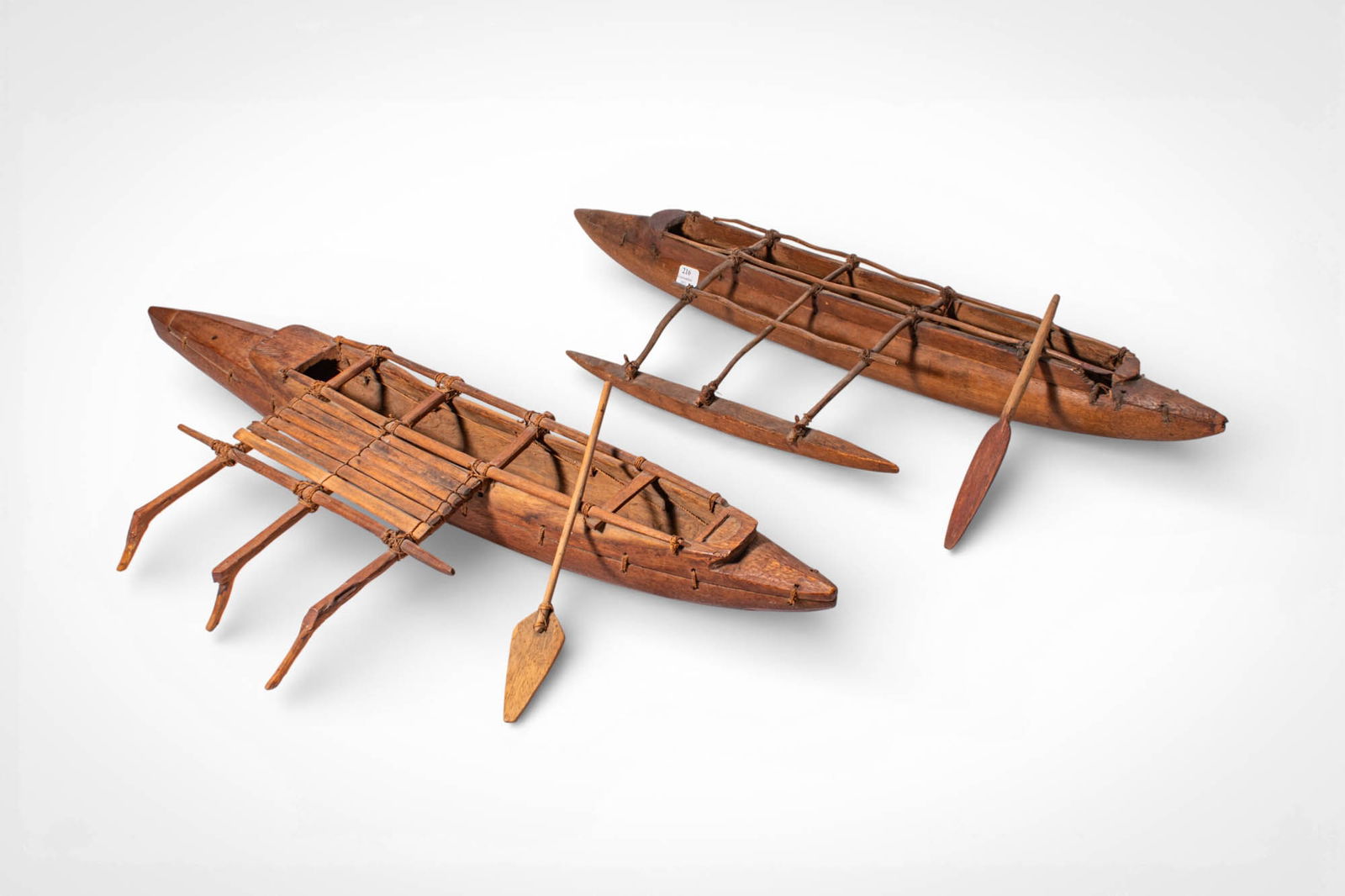 TWO POLYNESIAN CANOE MODELS: Ca. 20th century AD. >A group of two Polynesian canoe models, each carved from wood and fitted with miniature structural elements reflecting traditional ocean transportation. The elongated hulls are c