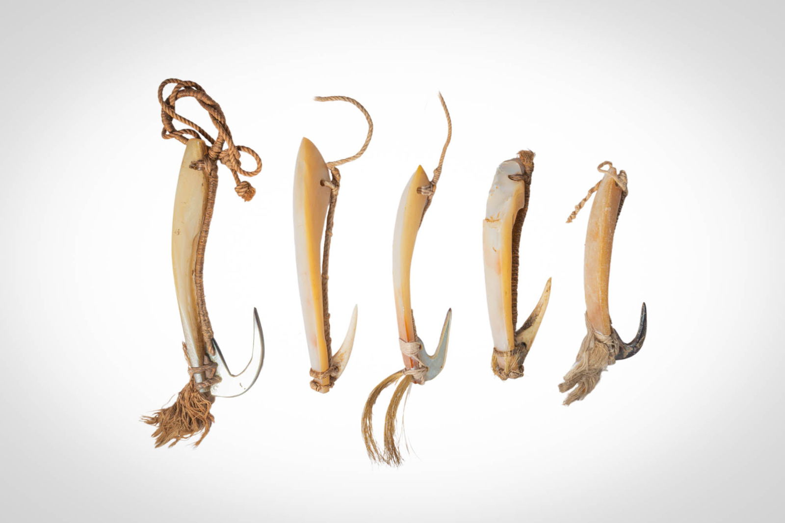 GROUP OF POLYNESIAN TROLLING LURES: Ca. 19th - 20th century AD. >A group comprising five elongated trolling lures carved from shell, each fitted with a hook secured by fibre lashings. The slender bodies taper toward pointed ends and ret