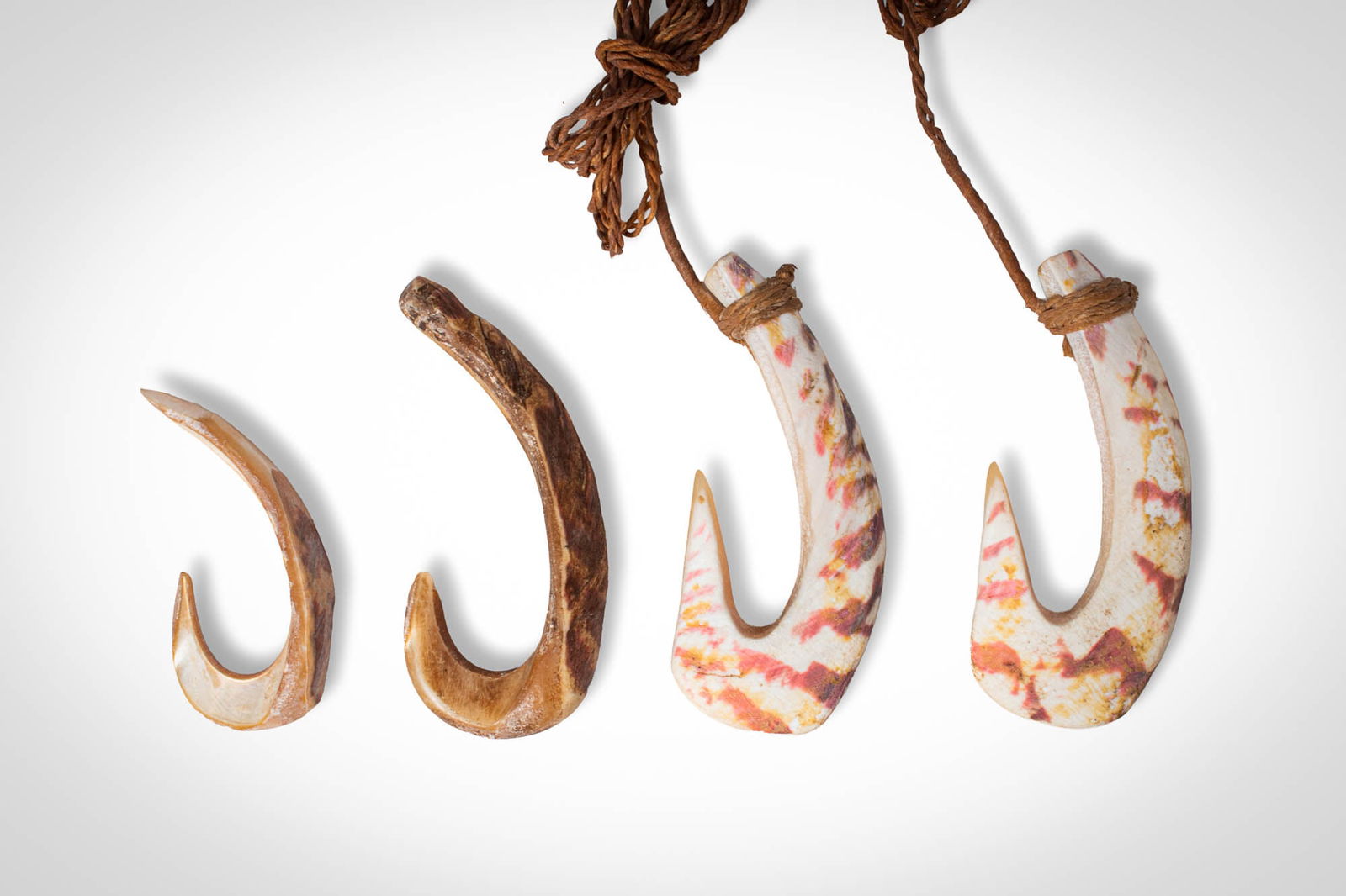 GROUP OF MATTY ISLAND FISH HOOKS: Ca. 19th - early 20th century AD. >A group comprising four fish hooks carved from shell, each formed with a broad, curved body tapering to a sharply pointed hook. Two examples retain fibre loops at th