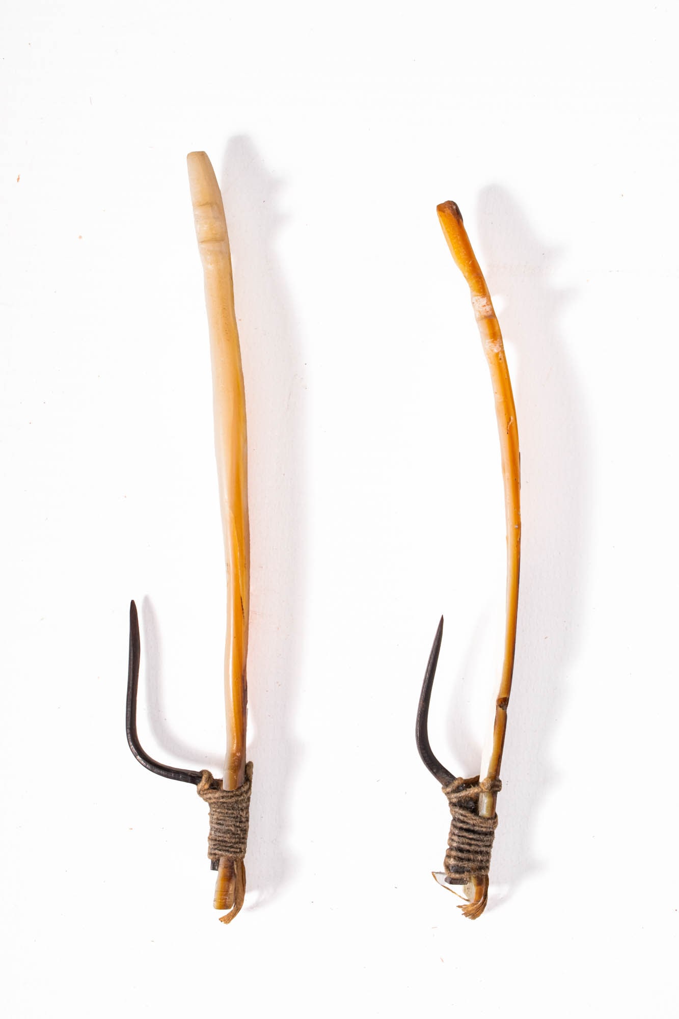 TWO OCEANIC FISH HOOKS: Ca. 19th century AD. A pair of Oceanic trolling hooks, each carved from iridescent mother-of-pearl shell with elegant finial-like terminals, bound with natural fibre to sharp bone points. These highly