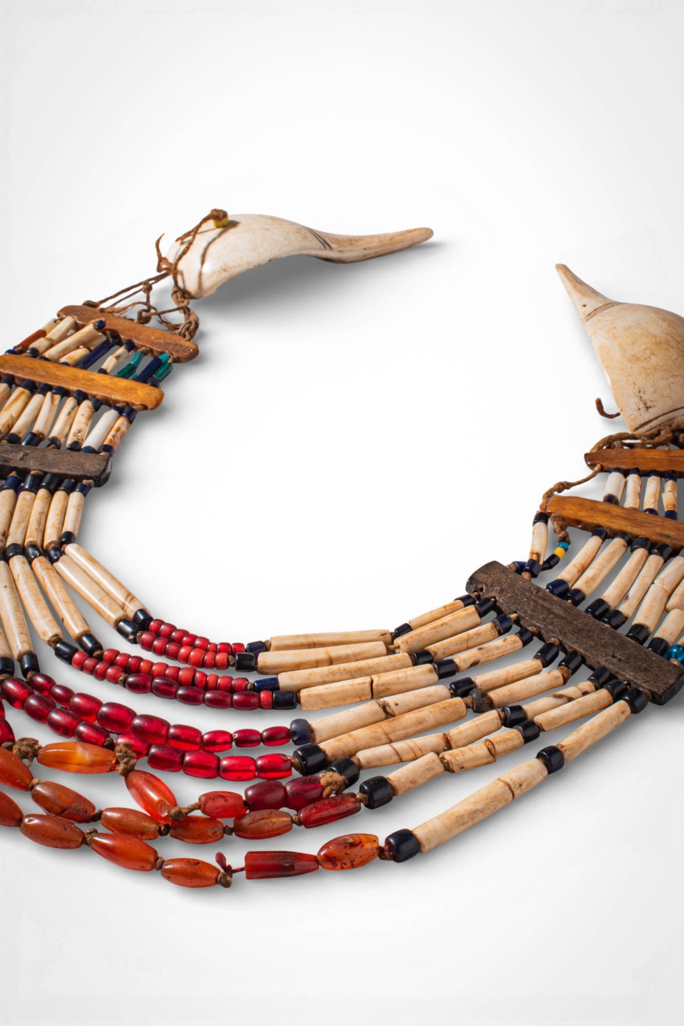 INDIAN NAGALAND POLYCHROME NECKLACE: Ca. 19th - 20th century AD. >A necklace composed of multiple suspended strands of elongated bone and glass beads, with carnelian beads arranged in alternating bands of cream, red and black. The strand
