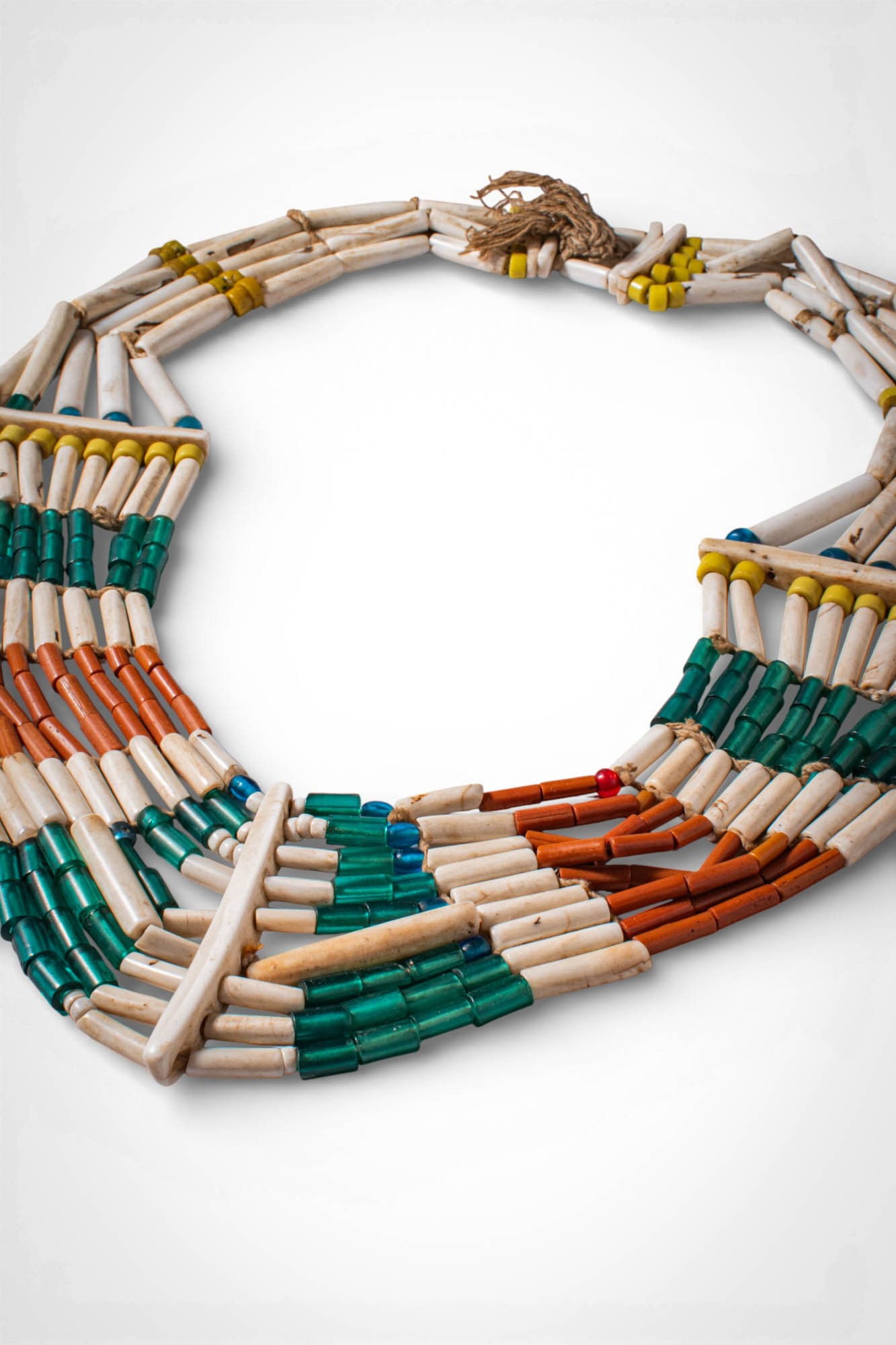 INDIAN NAGALAND POLYCHROME NECKLACE: Ca. 19th - 20th century AD. >A necklace composed of multiple strands of elongated shell beads interspersed with cylindrical glass beads in green, orange and white. The strands are arranged in a layere
