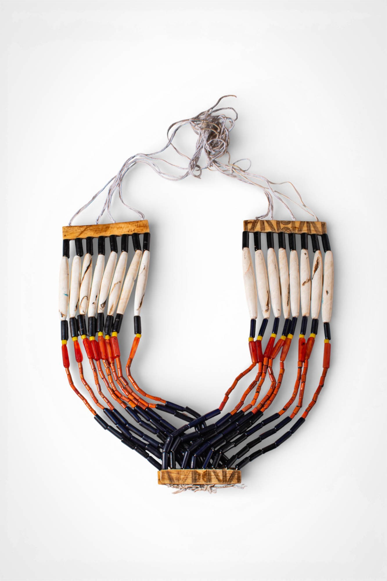 INDIAN NAGALAND POLYCHROME NECKLACE: Ca. 19th - 20th century AD. >A necklace composed of multiple suspended strands of elongated shell pendants and tubular carnelian and glass beads arranged in alternating bands of black, red, and orange