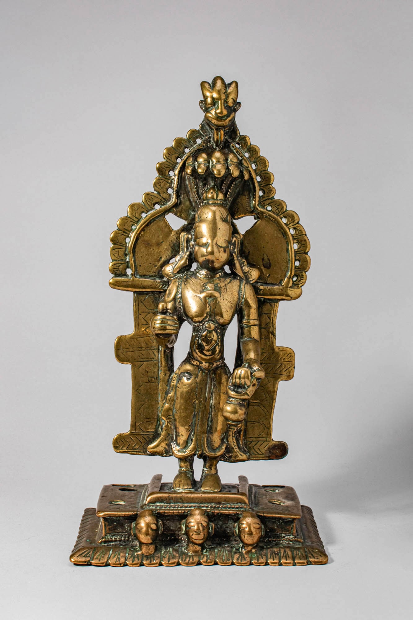 JAIN BRASS FIGURE OF PARSVANATHA: Ca. 17th-18th century AD. A cast brass figure of Jina Parsvanatha, the 23rd Tirthankara, standing upon a base adorned with three heads. The enlightened being is sheltered beneath a seven-hooded canopy