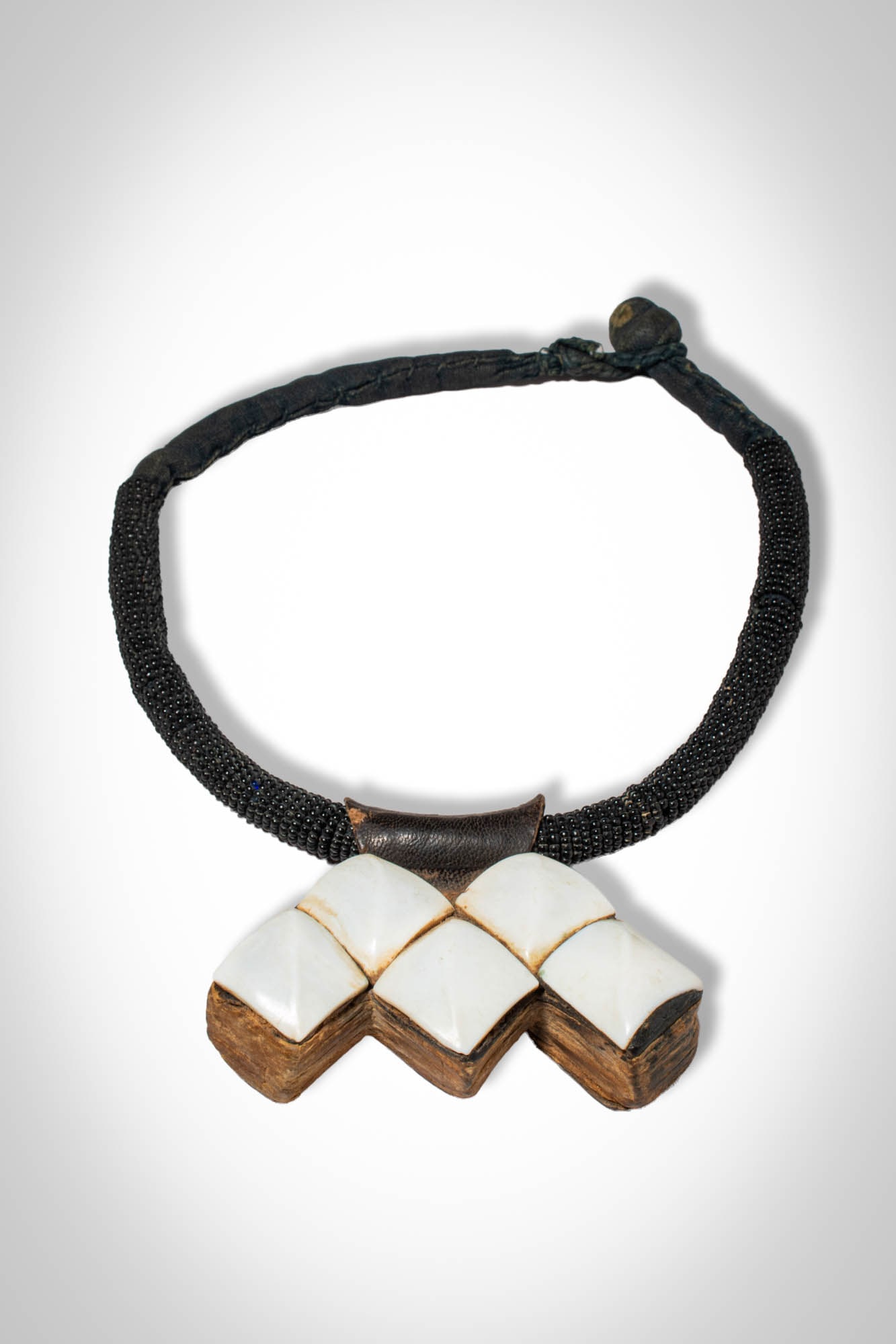 TUAREG NECKLACE: Ca. mid 20th century AD. >A Tuareg necklace composed of a strand of densely threaded dark beads forming a flexible collar, the necklace is centred by a fitting suspending a geometric pendant. Each squ