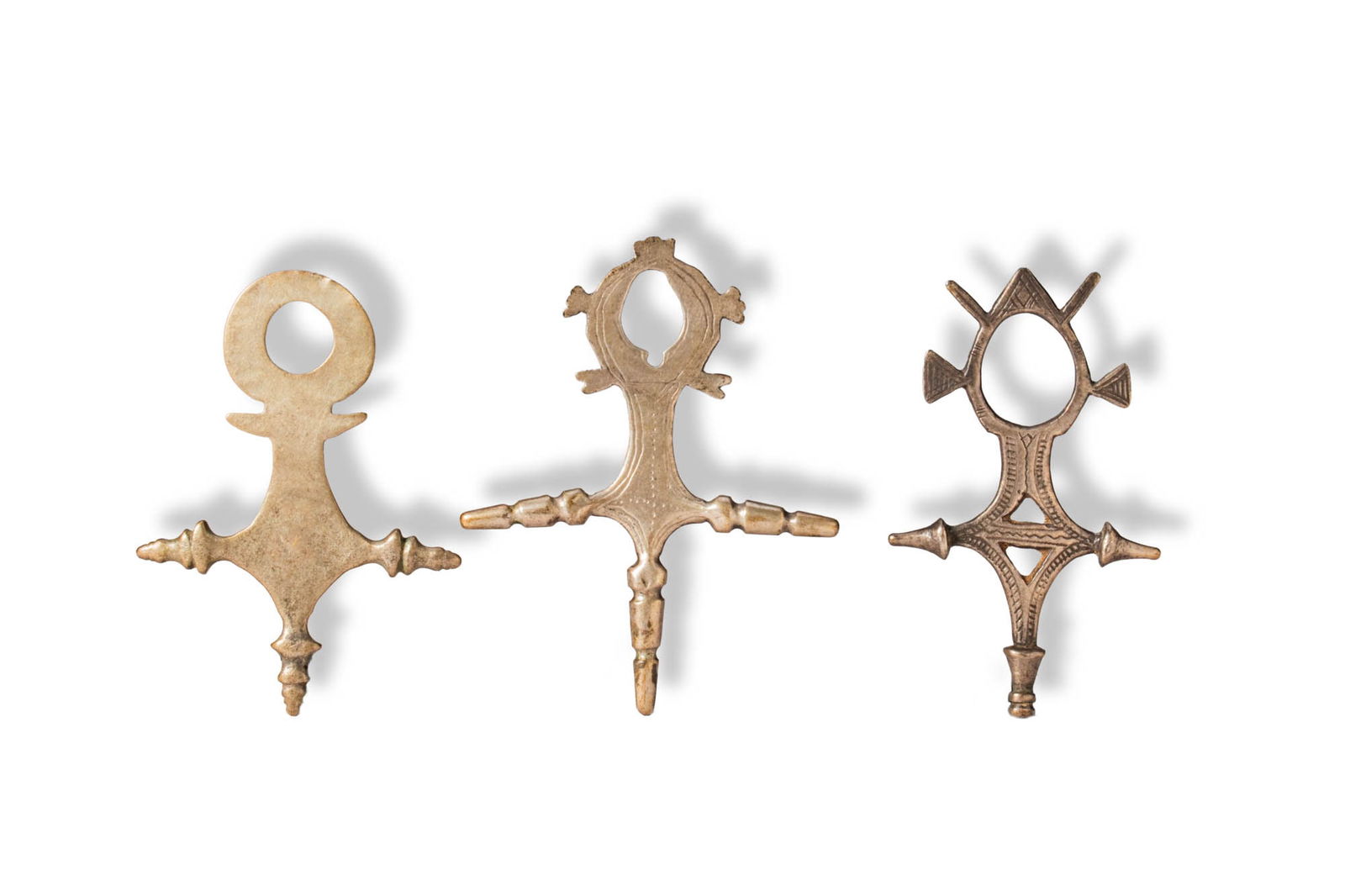 GROUP OF TUAREG ORNAMENTS: Ca. 19th - 20th century AD. >A group comprising three cast metal ornaments of openwork form, each featuring a circular or oval upper element surmounting a cross-shaped body. The surfaces are decorated