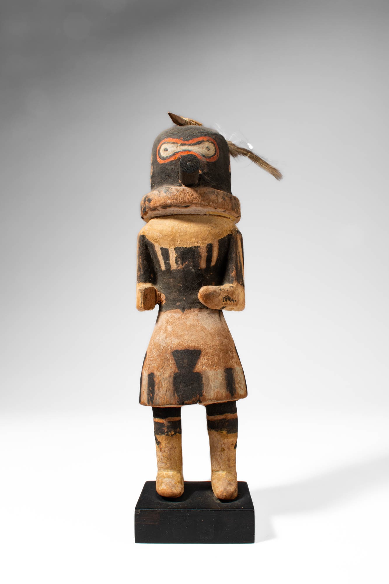 KACHINA HOPI DOLL: Ca. 20th century AD. >A Kachina Hopi doll with a cylindrical head and compact body, with contrasting fields of black and buff pigment. The face features a projecting nose and a goggle-like eye motif o