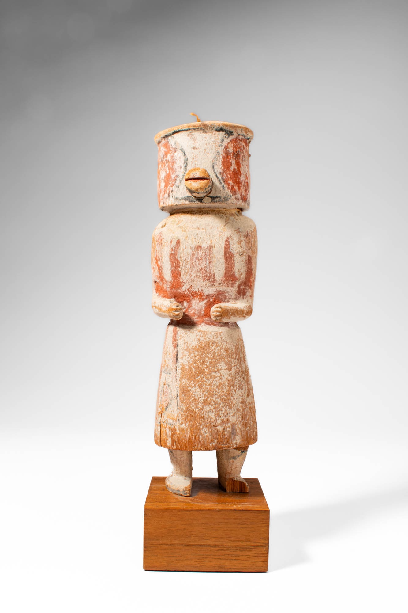 KACHINA HOPI DOLL: Ca. 20th century AD. >A Kachina Hopi doll with a cylindrical head and simplified body, the doll is decorated with traces of red and white pigment across the surface. The face features a projecting nos