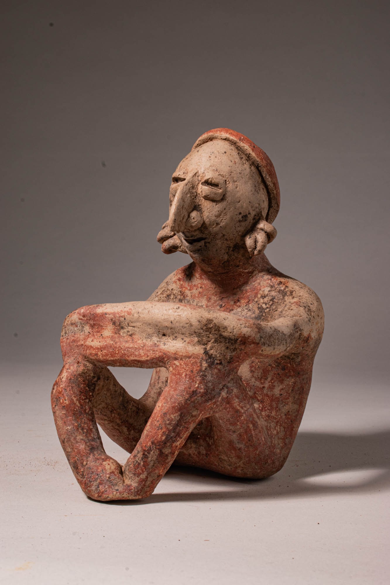 JALISCO POTTERY SEATED NUDE MALE FIGURE: Pre-Columbian, West Mexico, Jalisco, Ca. 3rd century BC - 3rd century AD. >A seated nude male figure, his body shaped with the gentle asymmetries and handmade softness that mark the finest Jalisco scu
