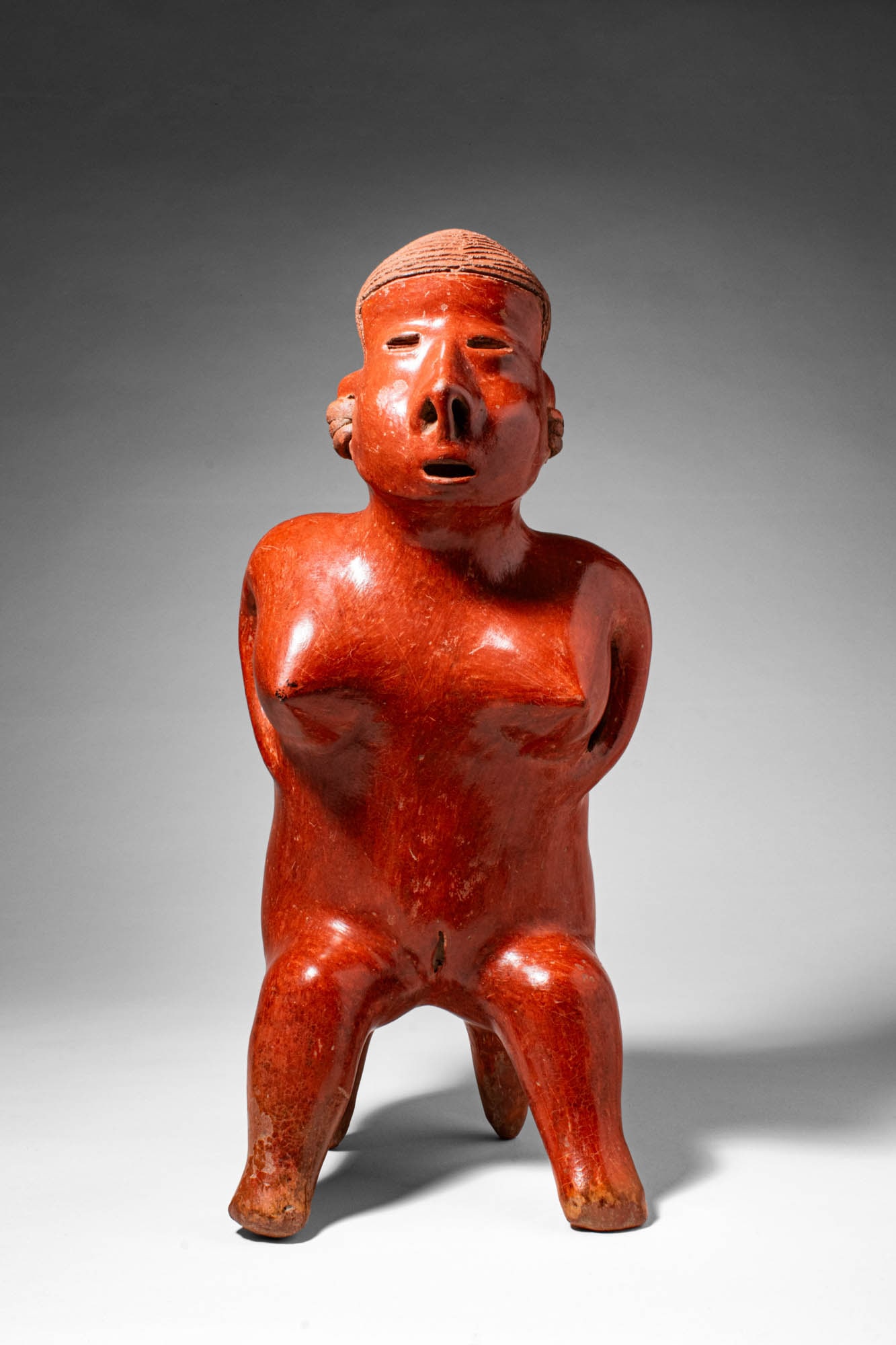 FINE NAYARIT SAN SEBASTIAN SEATED FIGURE OF NUDE FEMALE: Pre-Columbian, West Mexico, Nayarit, San Sebastian style, Ca. 3rd century BC - 3rd century AD. >A striking red-slipped pottery figure of a seated nude woman, modelled with the distinctive volumetric f