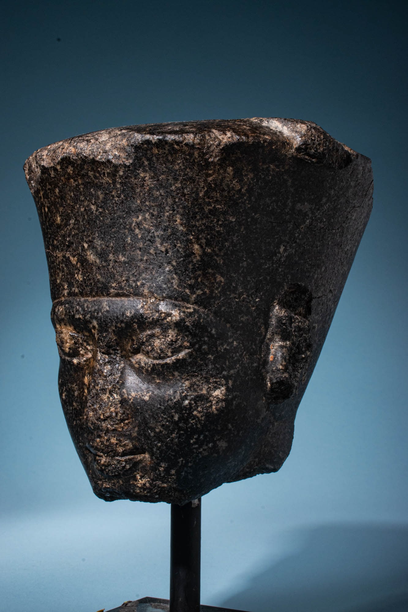 EGYPTIAN GRANODIORITE HEAD OF THE GOD AMUN WITH THE FEATURES OF KING TUTANKHAMUN: Late 18th Dynasty, Ca. 1336 - 1295 BC. A remarkably rare black stone (granodiorite) head of god Amun, with a braided beard and a flat cap. His small eyes are separated by a curved depression from the