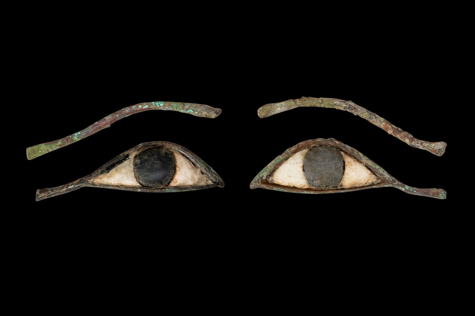 PAIR OF EGYPTIAN EYE INLAYS AND EYEBROWS: Late Period, Ca. 664 - 30 BC. A matching set of mummy inlays comprising a pair of eyes and brows. Each eye is constructed from a bronze frame with a white stone sclera and a circular black stone iris.