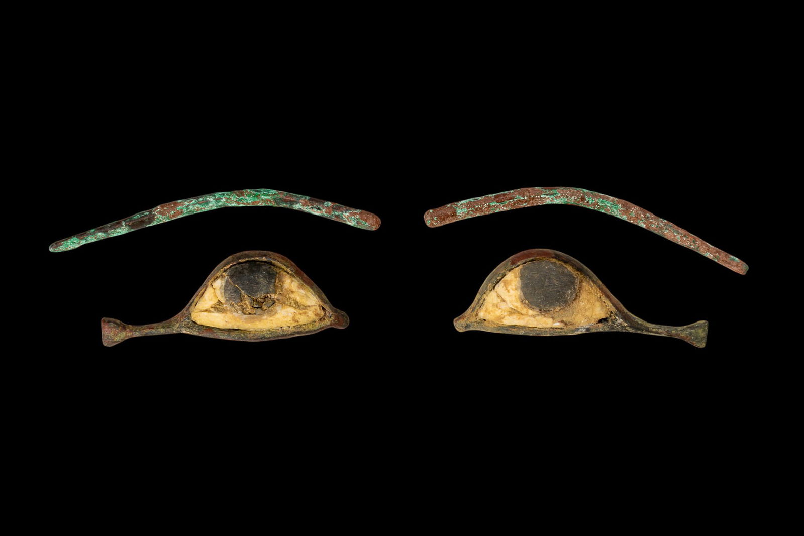 PAIR OF EGYPTIAN EYE INLAYS AND EYEBROWS: Late Period, Ca. 664 - 30 BC. A matching set of mummy inlays comprising a pair of eyes and brows. Each eye is constructed from a bronze frame with a white stone sclera and a circular black stone iris.