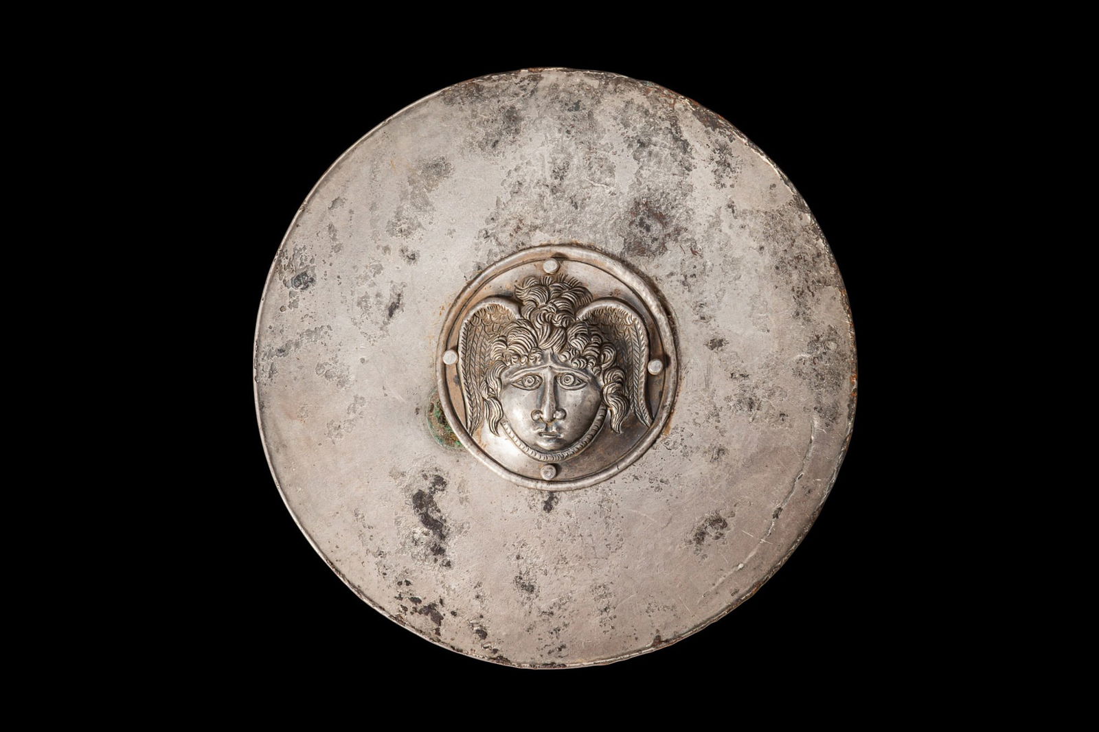 GREEK SILVER PHALERA WITH GORGON: Ca. 400 - 200 BC. A silver phalera formed as a circular plaque riveted at the centre with a high-relief roundel showing a gorgon with staring eyes, a broad nose, and a closed mouth. The hair is render