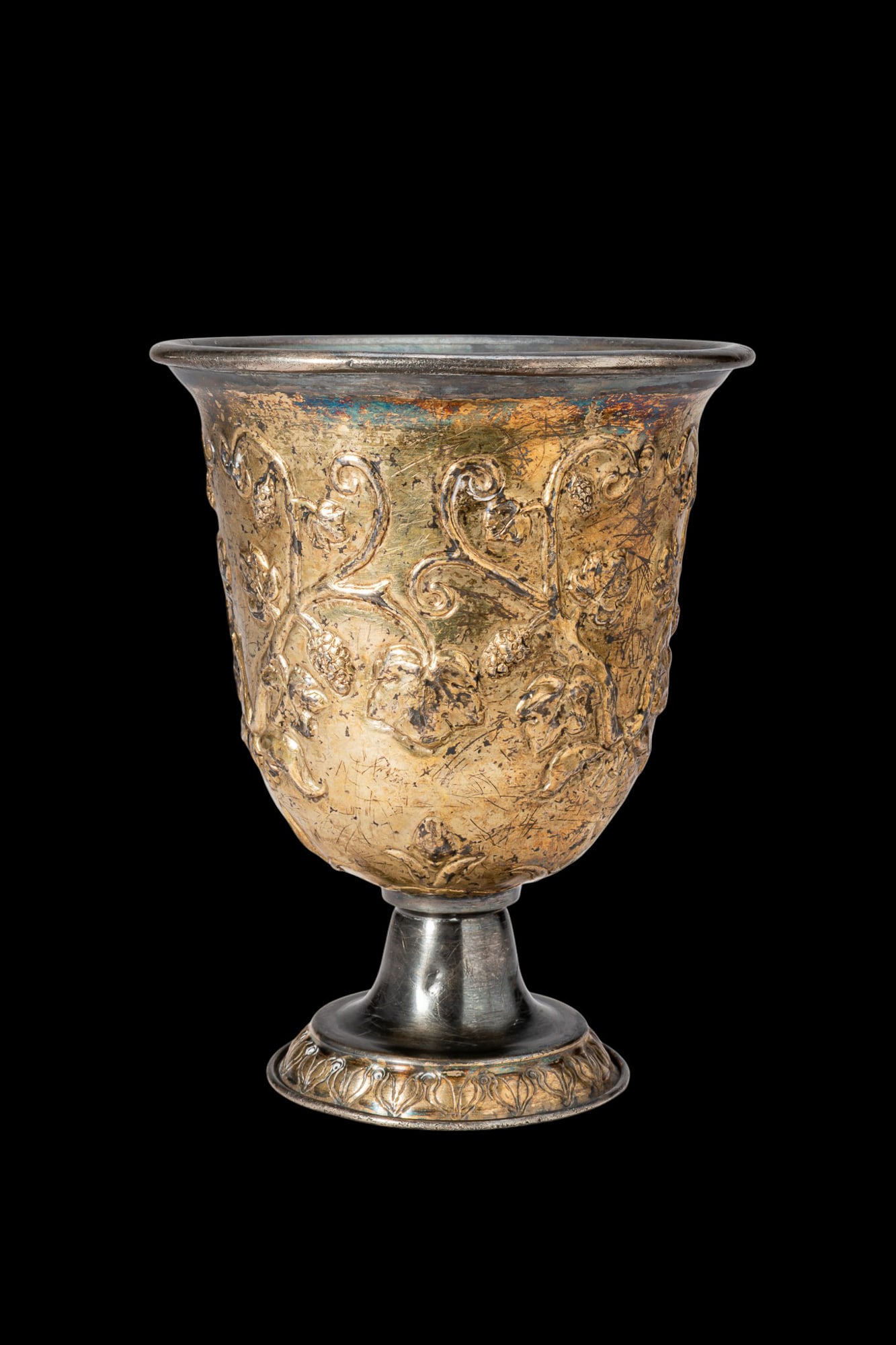 ROMAN PARCEL GILT SILVER PEDESTAL CUP WITH VINE TENDRILS: Ca. AD 100 - 400. A pedestal cup formed with a double wall. The body rises from a concave foot on a short stem and flares to a broad, everted rim. The outer wall is gilt and chased with scrolling vine