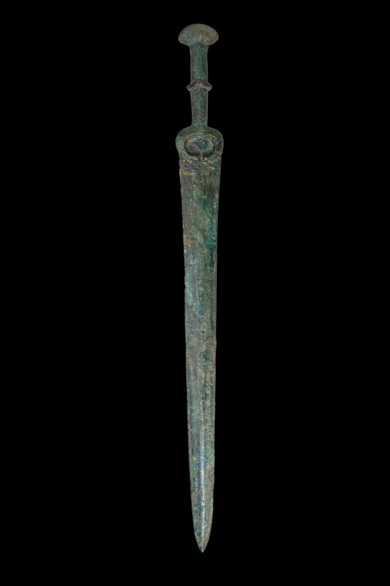 BRONZE AGE / EARLY GREEK PERIOD BRONZE DAGGER: Ca. 1200 - 800 BC. A cast bronze dagger with a long, straight blade tapering to a sharp point, and a hilt with a crescent-shaped guard, a cylindrical grip with a moulded ring, and a rounded pommel. Si