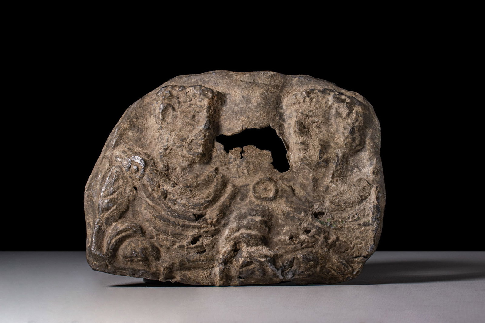 ROMAN LEAD SARCOPHAGUS PLAQUE DEPICTING TWO EMPERORS: Ca. AD 100 - 150. A cast lead plaque of ovoid outline in low relief, presenting two confronting imperial busts with short curled hair and well-defined features. Each wears a mantle arranged in concent