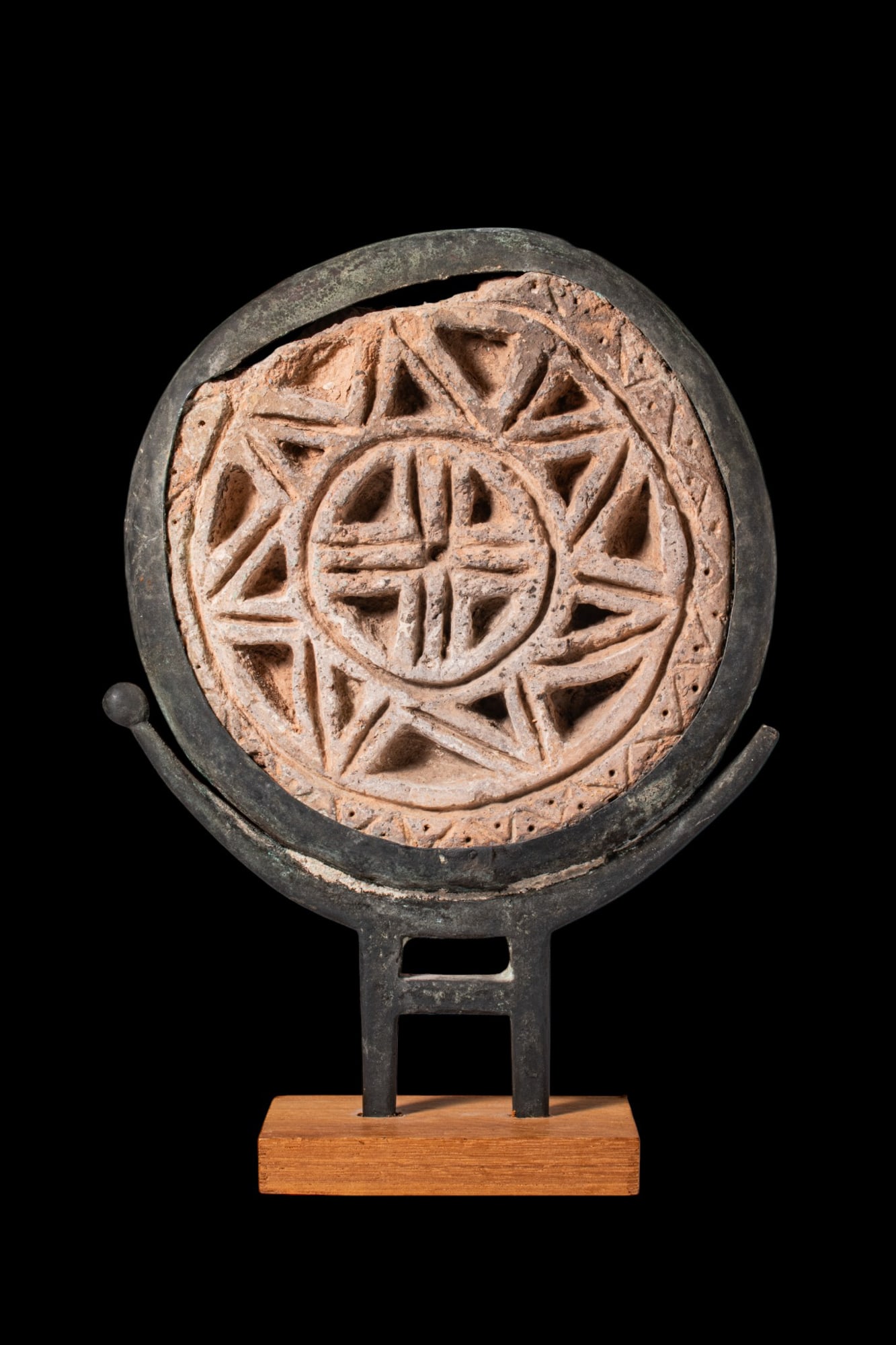 BYZANTINE LIMESTONE ARCHITECTURAL ROUNDEL WITH CROSS IN BRONZE FRAME: Ca. AD 500 - 800. A limestone architectural roundel set within a circular cast bronze frame. One face is carved with a central cross within a roundel, encircled by radiating triangular compartments. T