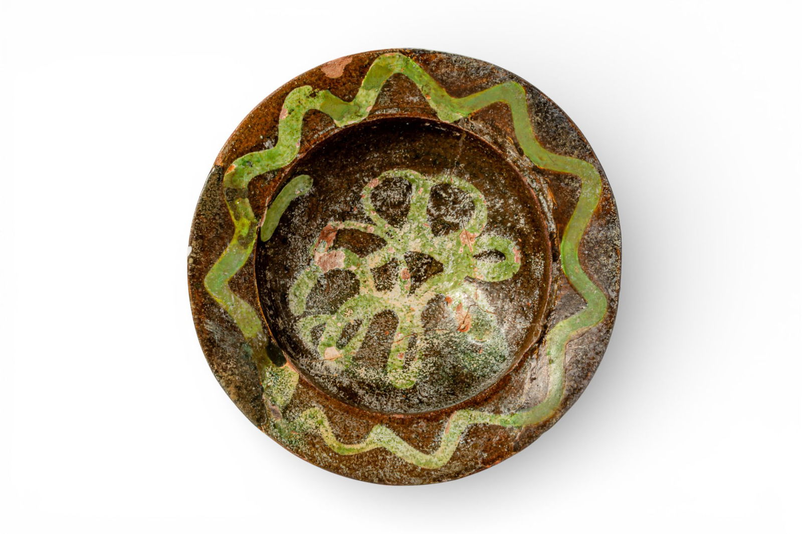 BYZANTINE GLAZED EARTHENWARE FOOTED DISH WITH GREEN WAVY BAND AND CENTRAL MOTIF - EX ASHMOLEAN MUSEU: Ca. AD 1300 - 1400. A glazed earthenware footed dish with a shallow well set above a short pedestal foot. The interior is coated in a brown glaze and decorated with a green wavy band running around th