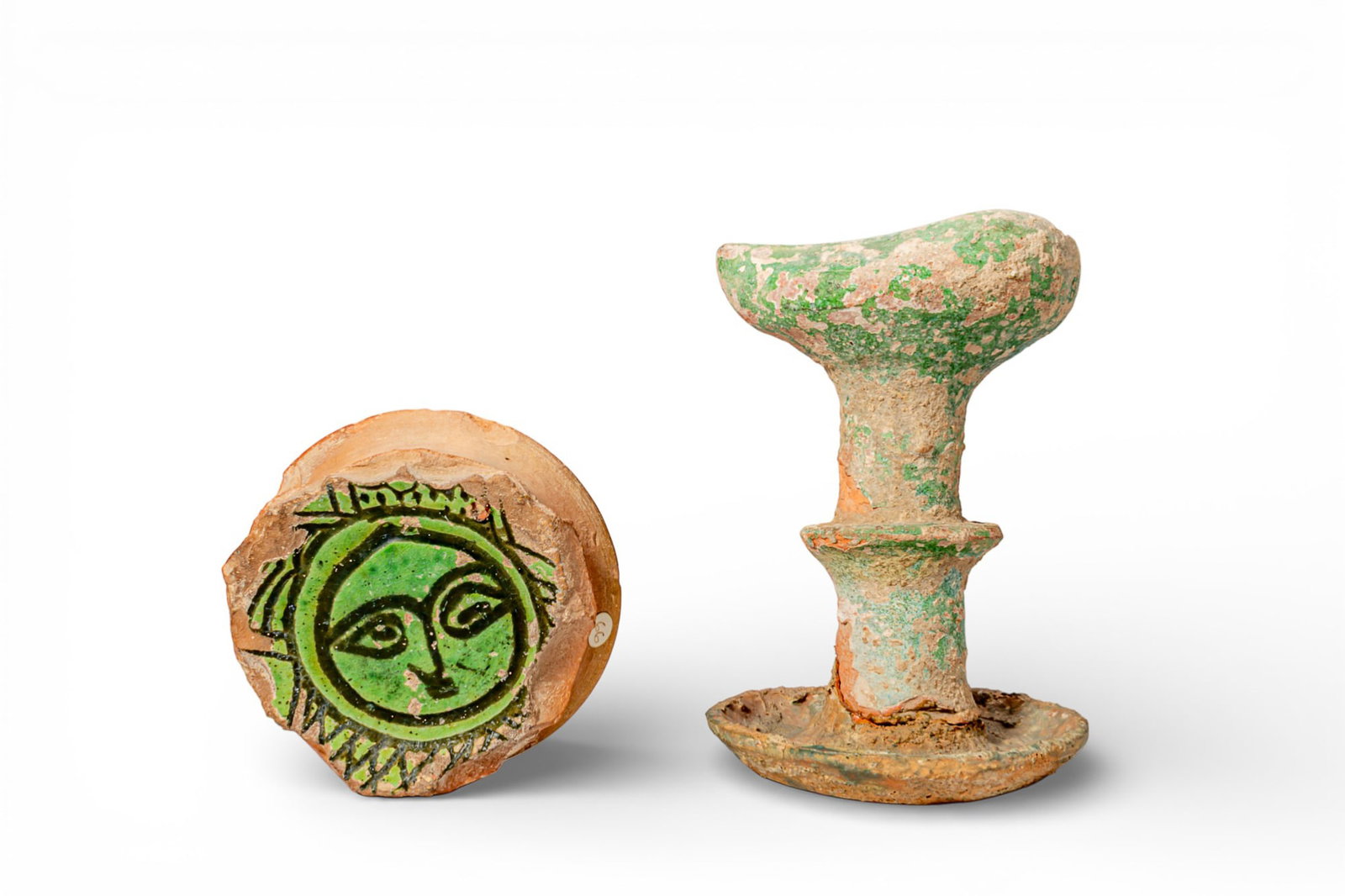 MEDIEVAL ISLAMIC GREEN-GLAZED TERRACOTTA OIL LAMP AND BOWL TONDO - EX ASHMOLEAN MUSEUM: Ca. AD 1300 - 1400. A pair of terracotta objects, including: a circular bowl tondo fragment, the upper face slightly recessed, with a green-glazed roundel painted in black with a stylised frontal face