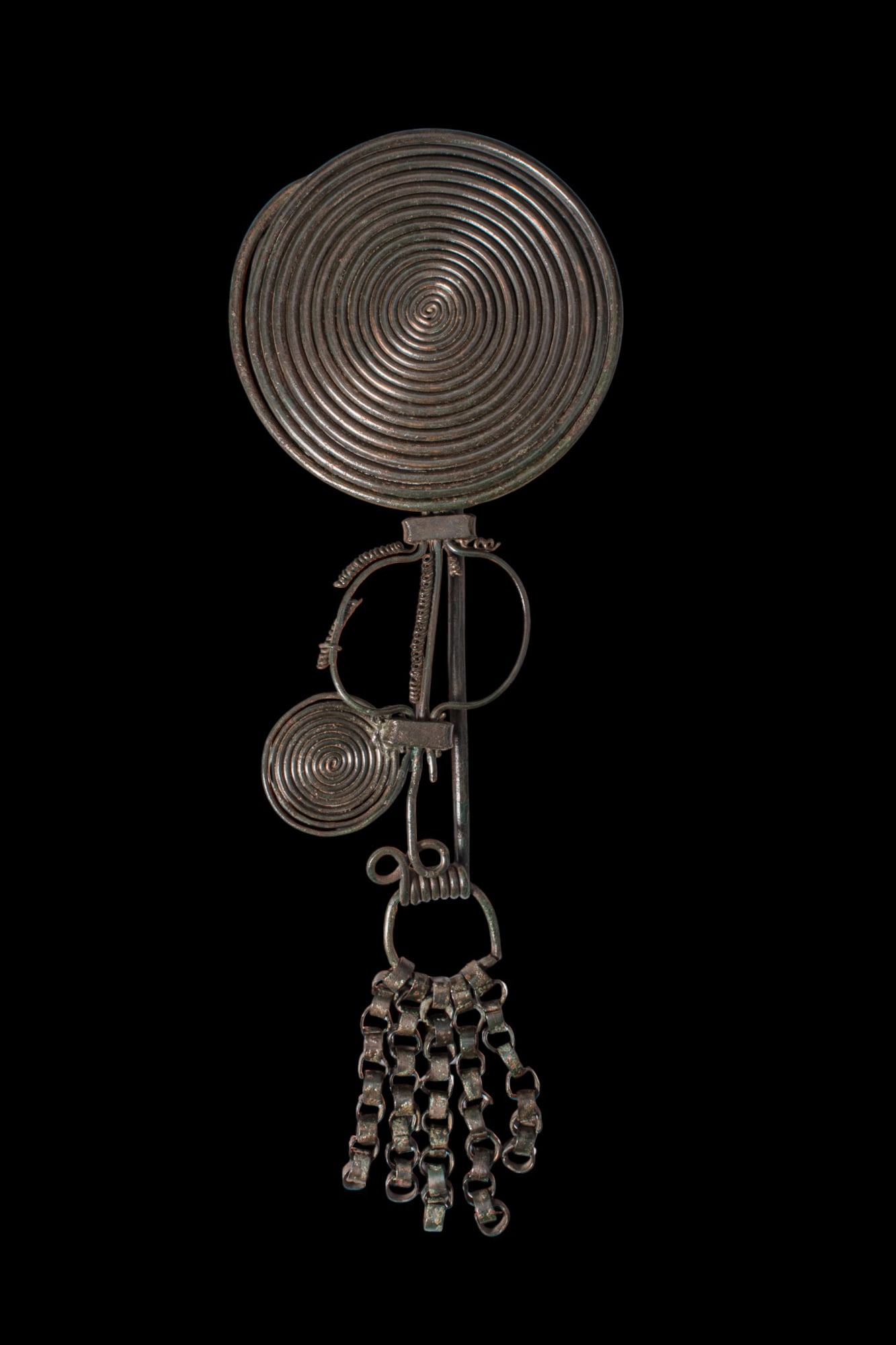 LARGE HALLSTATT BRONZE SPIRAL FIBULA: Ca. 1300 - 1000 BC. A large bronze fibula with a broad spiral plate formed from tightly coiled wire, the coils terminating at the lower edge above a rectangular junction for the spring and pin. The bo