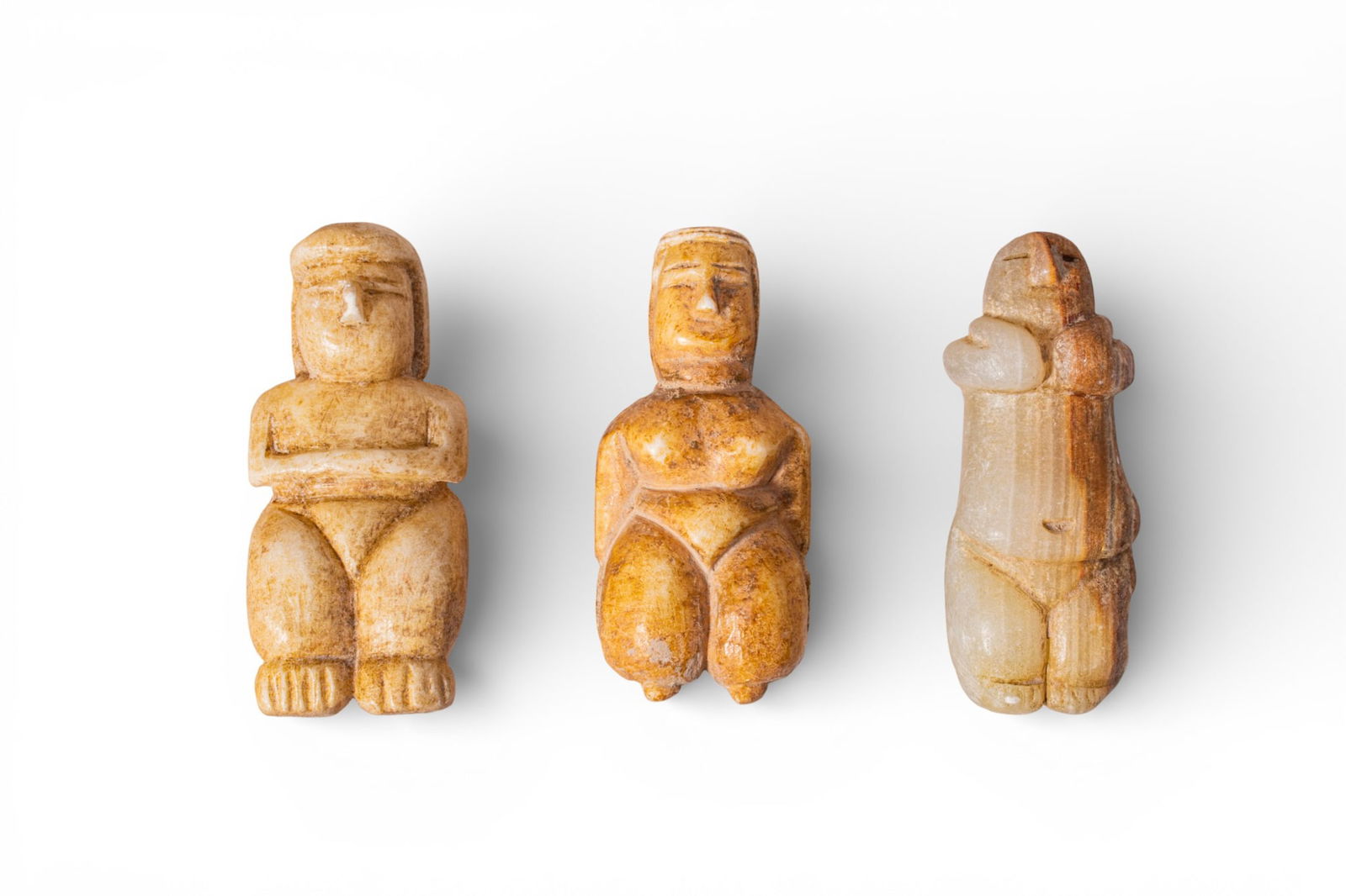 COLLECTION OF SOUTH ARABIAN ALABASTER GODDESS IDOLS: Ca. 300 - 100 BC. A collection of three goddess idols, including, from left to right: a squat figure with a cuboid head and schematised facial features, the arms folded across the chest above broad th