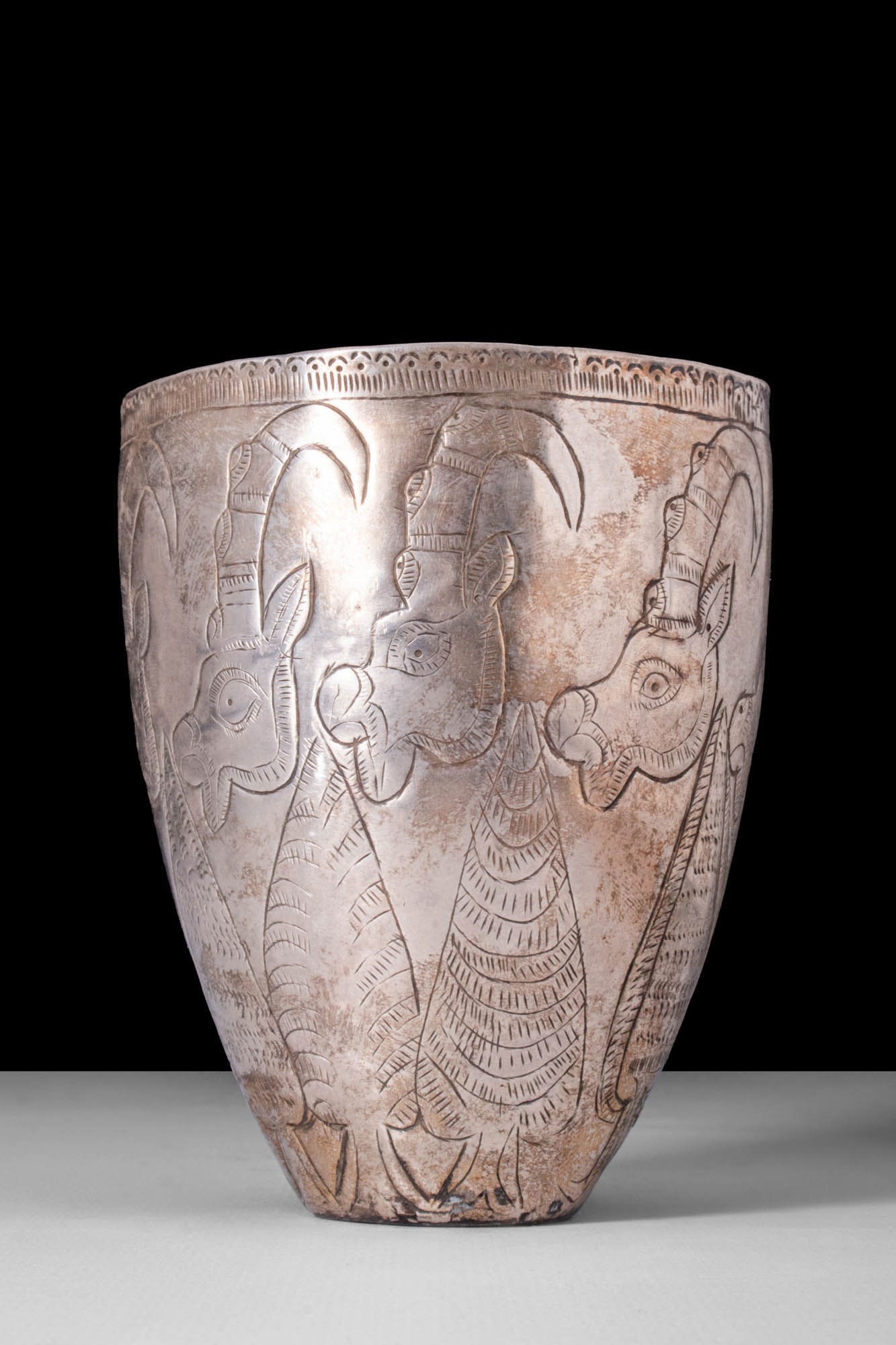 RARE ELAMITE SILVER BEAKER WITH PROCESSION OF RAM HEADS: Ca. 2700 - 1500 BC. A well-formed silver elamite beaker with an intricate incised decoration. The vessel features a frieze of stylised rams or ibexes on its exterior. These are distinctive Iranian mot