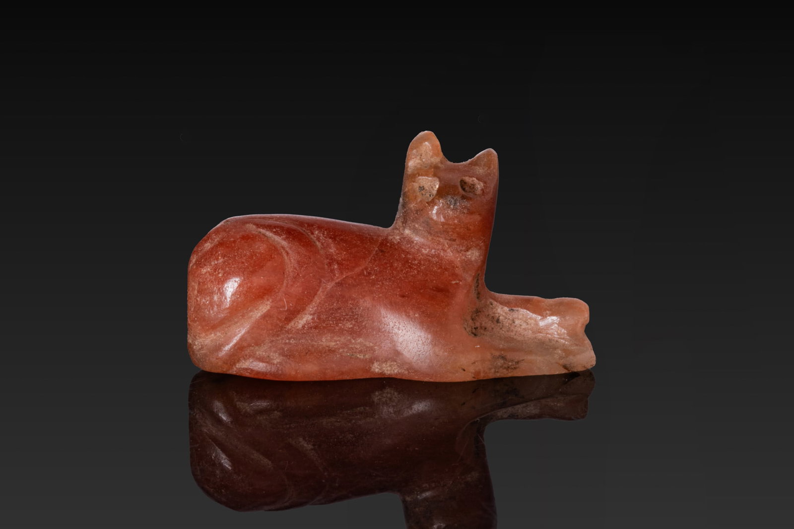 EGYPTIAN CARNELIAN CAT AMULET: New Kingdom, Ca. 1550 - 1069 BC. A carnelian amulet carved in the form of a recumbent cat with its forelegs extended and head raised. For similar see: The Israel Museum, Jerusalem, Accession number: 2