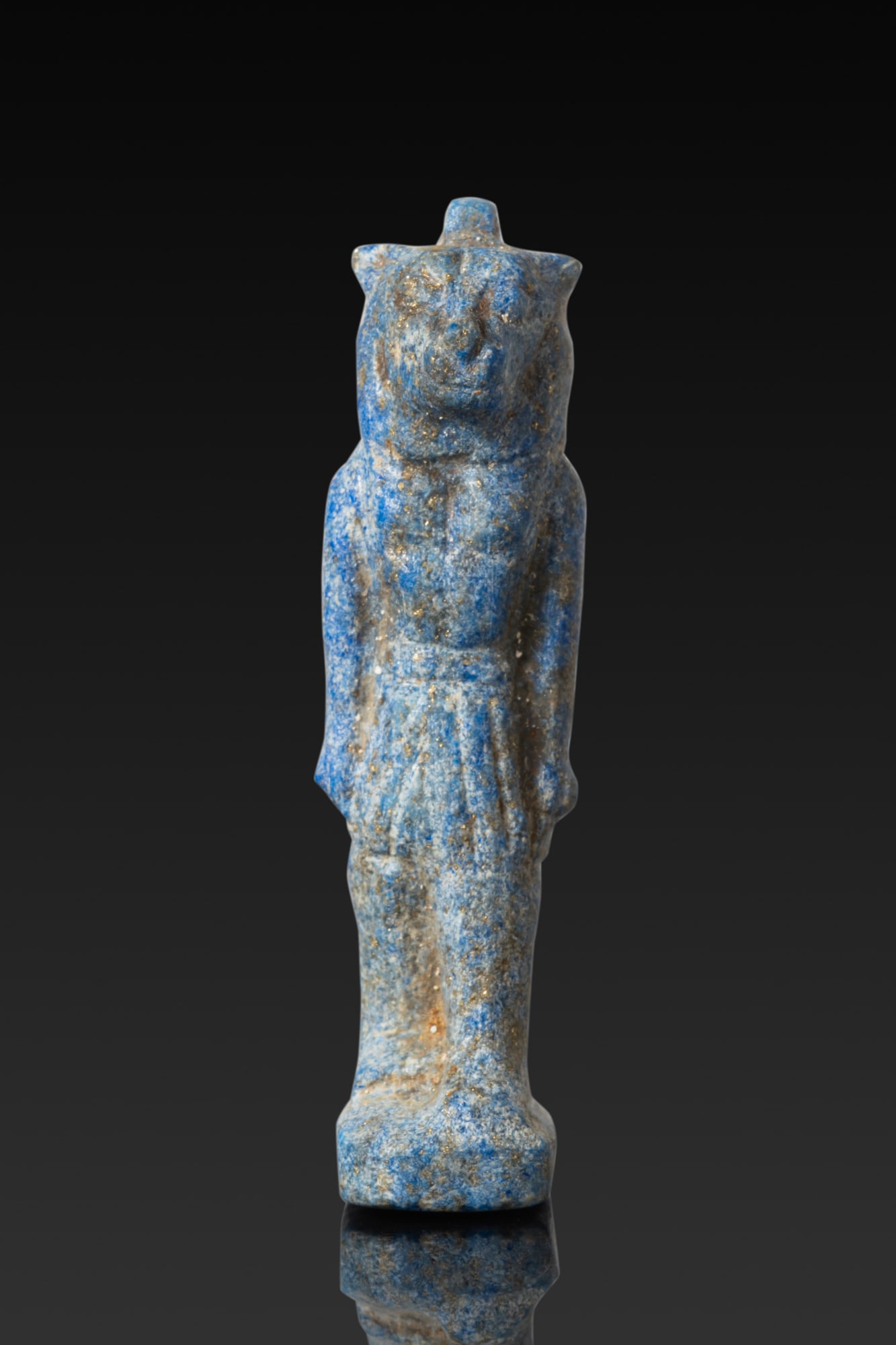 EGYPTIAN LAPIS LAZULI FIGURINE: Late Period to Ptolemaic Period, Ca. 664 - 30 BC. A lapis lazuli figurine of a lioness-headed deity, standing on an integral rectangular base with one leg advanced, bare-chested and wearing a pleated