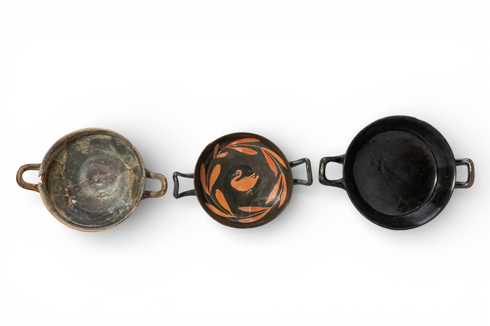 COLLECTION OF GREEK BLACK-GLAZED KYLIXES: Ca. 400 - 275 BC. A collection of three black-glazed kylikes, including, from left to right: a shallow cup on a tall stem and spreading foot, with a broad offset rim and horizontal handles; a shallow