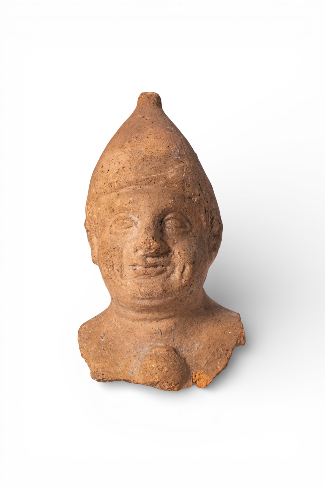 CYPRIOT TERRACOTTA BUST OF A PRIEST: Ca. 500 - 300 BC. A hollow terracotta bust of a priest, modelled with the head in a tall conical cap with a rounded tip. The face has almond-shaped eyes, a straight nose, and a closed mouth with a sli