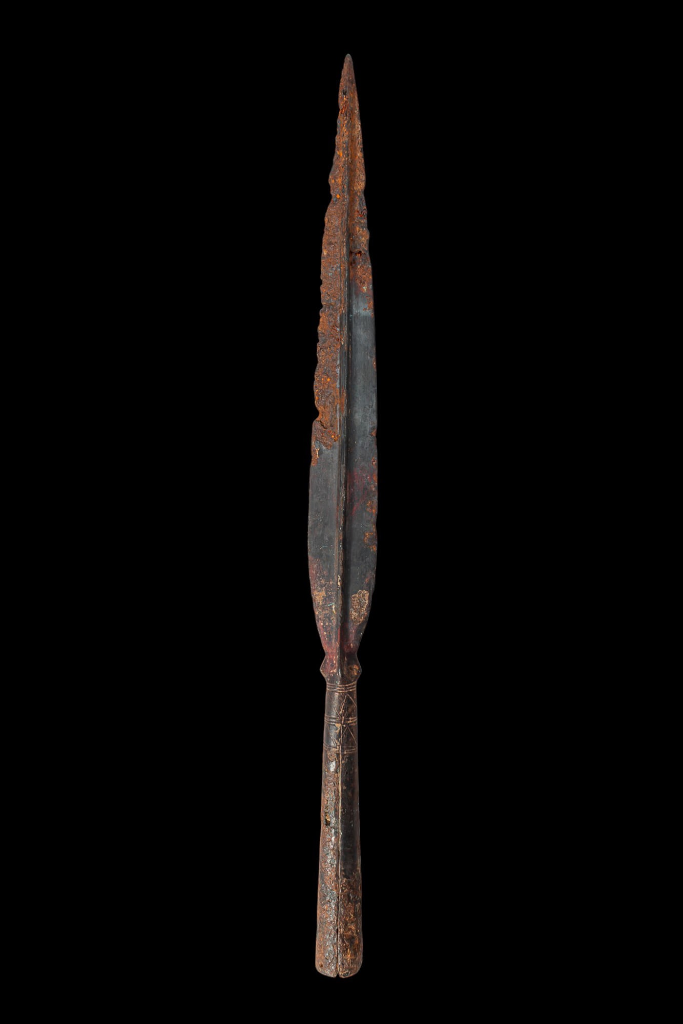LA TENE / CELTIC IRON SPEARHEAD: Ca. 450 BC. An iron spearhead with a long, narrow leaf-shaped blade and a pronounced central midrib. The blade narrows to a short shoulder above a cylindrical socket with incised bands around the