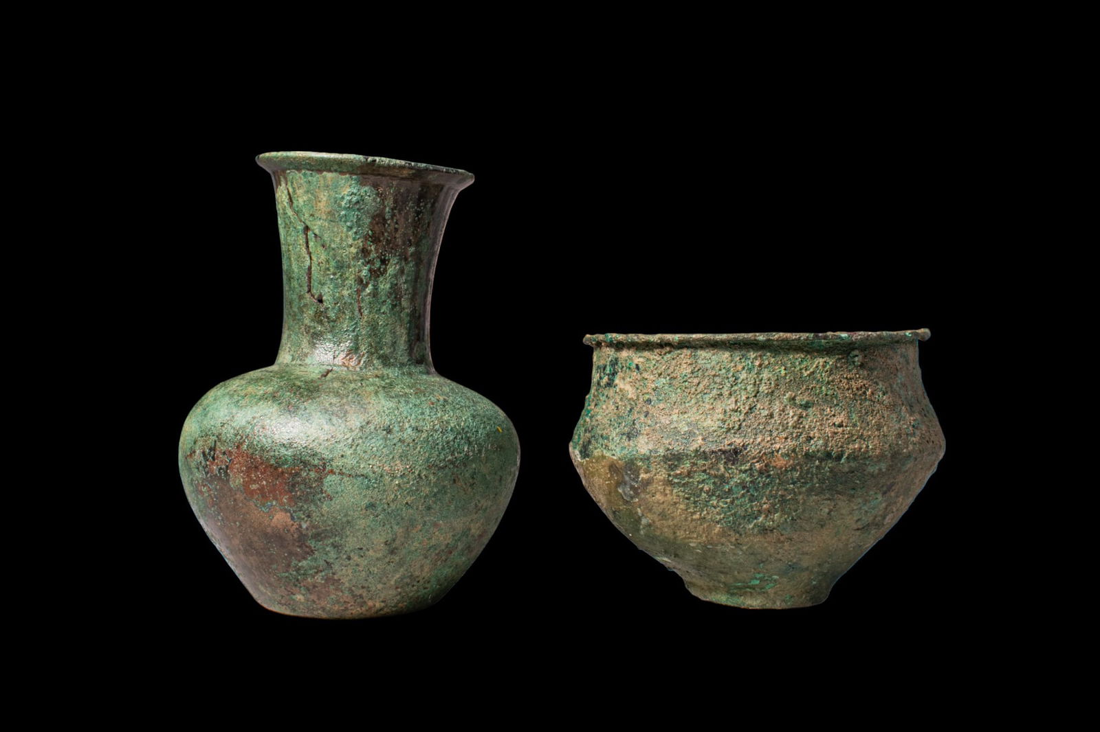 PAIR OF GREEK PERIOD BRONZE VESSELS: Ca. 500 BC. A pair of bronze vessels, from left to right: a vase with a globular body on a flat base, a broad shoulder, and a tall, cylindrical neck flaring to an everted mouth; and a jar with a