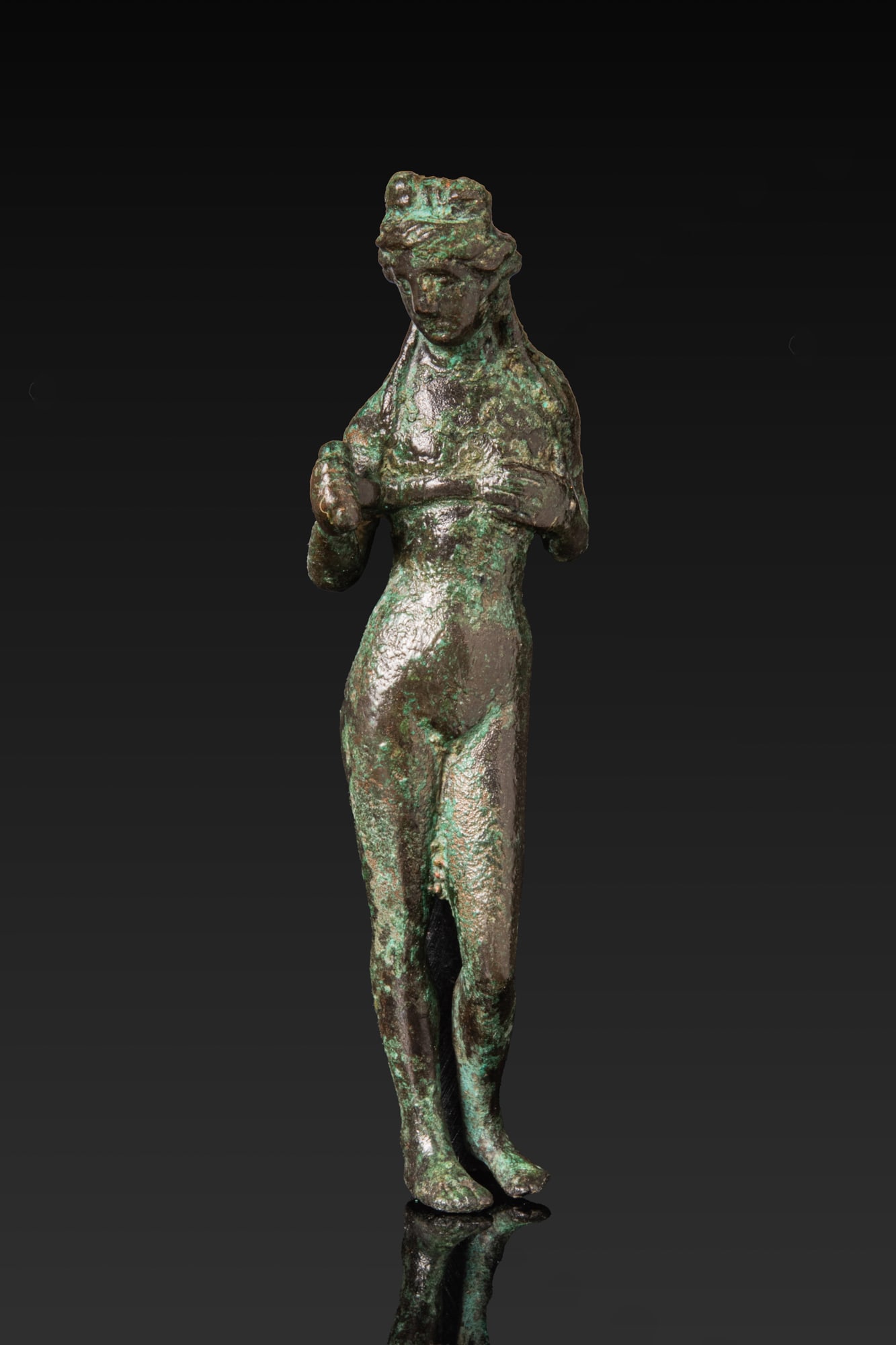 ROMAN BRONZE FIGURINE OF VENUS AT THE BATH: Ca. AD 1 - 300. A bronze figurine of a nude Venus, shown with the weight on the right leg and the head slightly inclined. The hair is gathered into an elaborate coiffure with loose strands falling ont