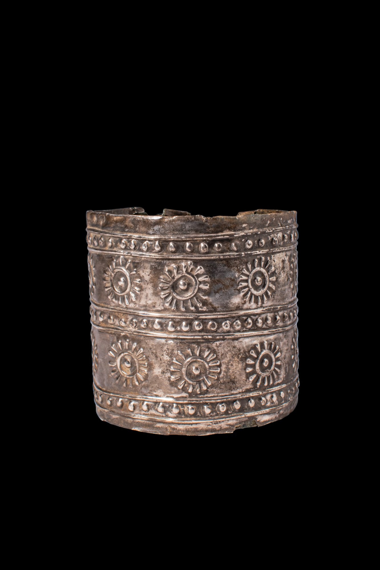 ROMAN SILVER CUFF BRACELET WITH ROSETTES: Ca. 100 BC - AD 100. A silver cuff bracelet formed as a broad band with an open back, the terminals pierced with round holes for fastening. The exterior decoration is arranged in two horizontal regist